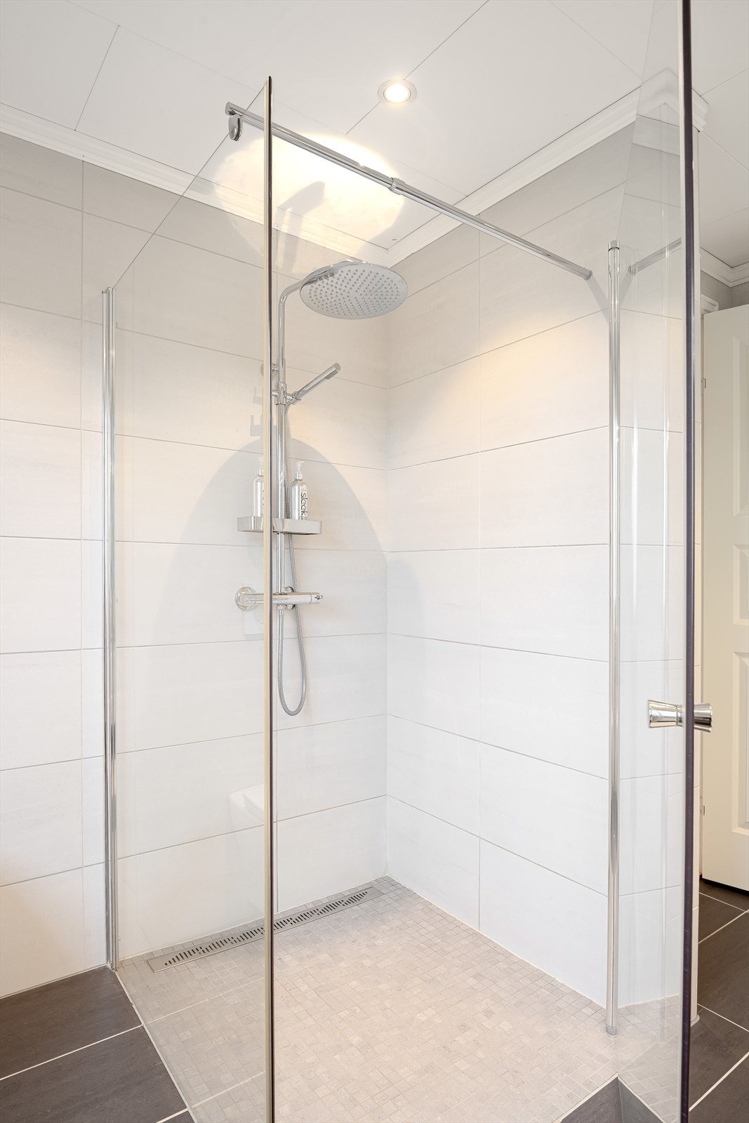 Baderommet har mørke fliser på gulv med gulvvarme, lyse fliser på veggene, downlights i himlingen og mekanisk avtrekk. Galleribilde