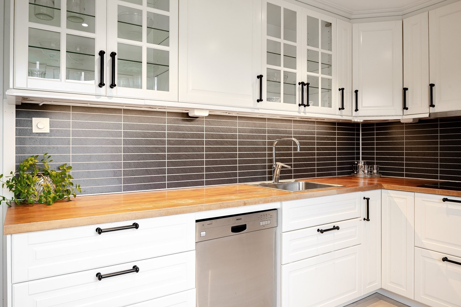 Praktisk med flisimitasjonsplater i benkeryggen og takhøye overskap med belysning under. Galleribilde