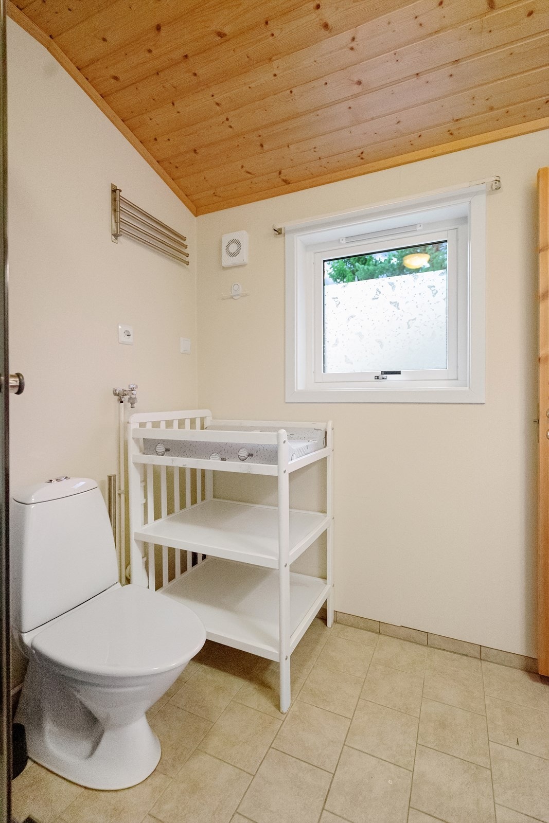 Et funksjonelt bad med flislagt gulv, panel i himling og vindu som slipper inn naturlig lys Galleribilde