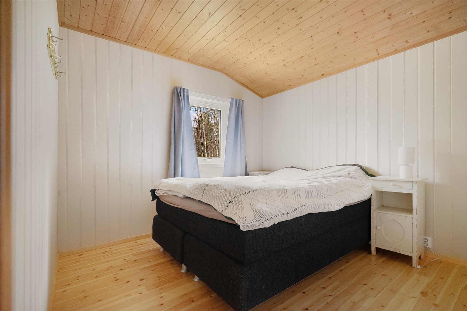 Lyst og lunt soverom med panelte vegger og tregulv som gir ekte hyttefølelse. Her våkner du til stillheten og utsikten mot naturen rett utenfor vinduet Galleribilde