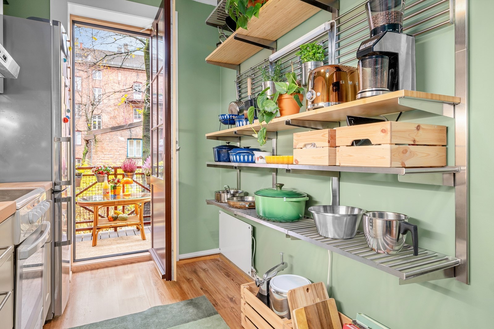 Ved å innrede med åpne hyller på den ene veggen får man mer luft og åpenhet på kjøkkenet. Det følger med en frittstående komfyr med keramisk platetopp, oppvaskmaskin og kjøl/frys. Galleribilde