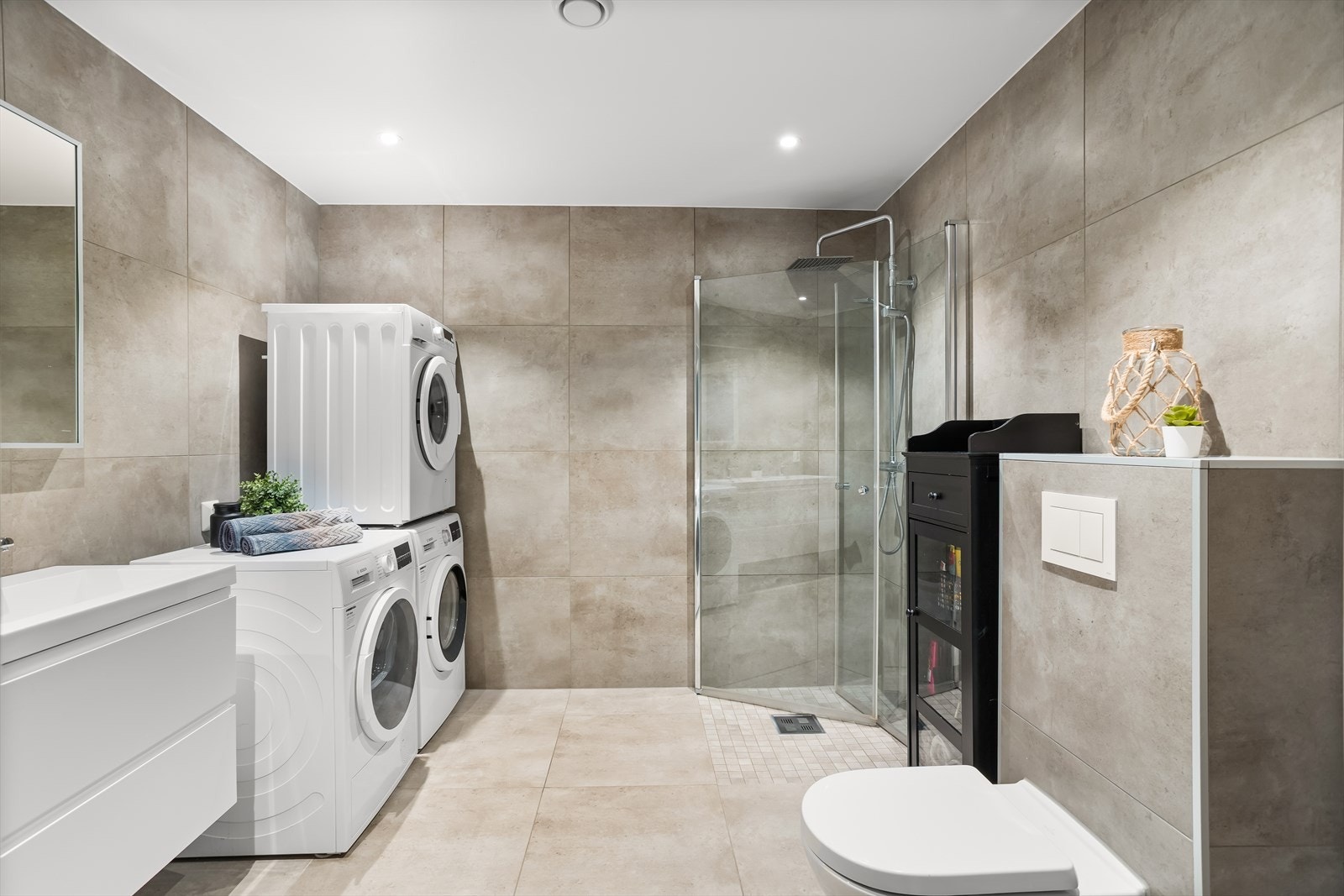 Badet er innredet med dobbelservant med underskap, speil, vegghengt toalett, dusjdører og opplegg til vaskemaskin. Galleribilde