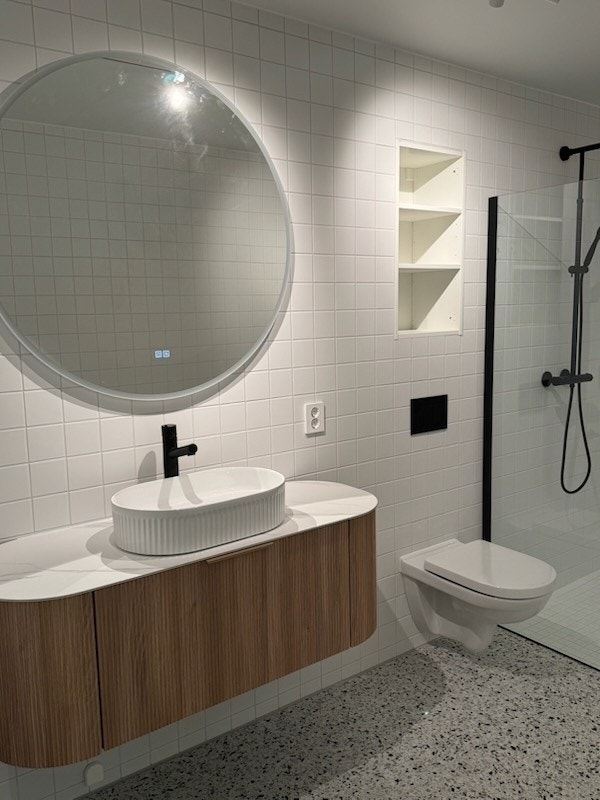 Stort bad med dusjhjørne, vegghengt toalett, servant, speil, vaskemaskin. Galleribilde