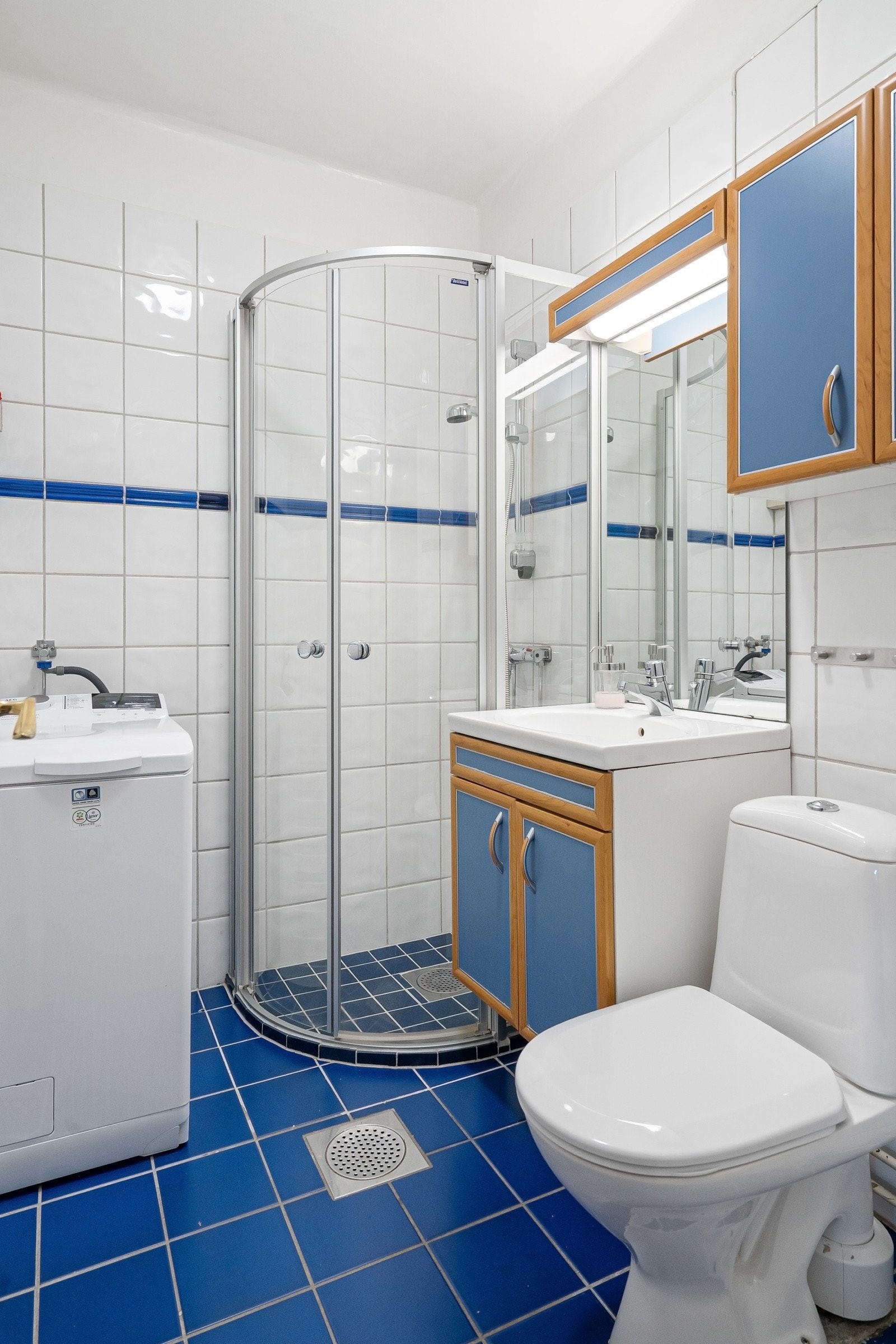 Lyst flislagt baderom med dusjhjørne, godt med skapplass og opplegg for vaskemaskin Galleribilde