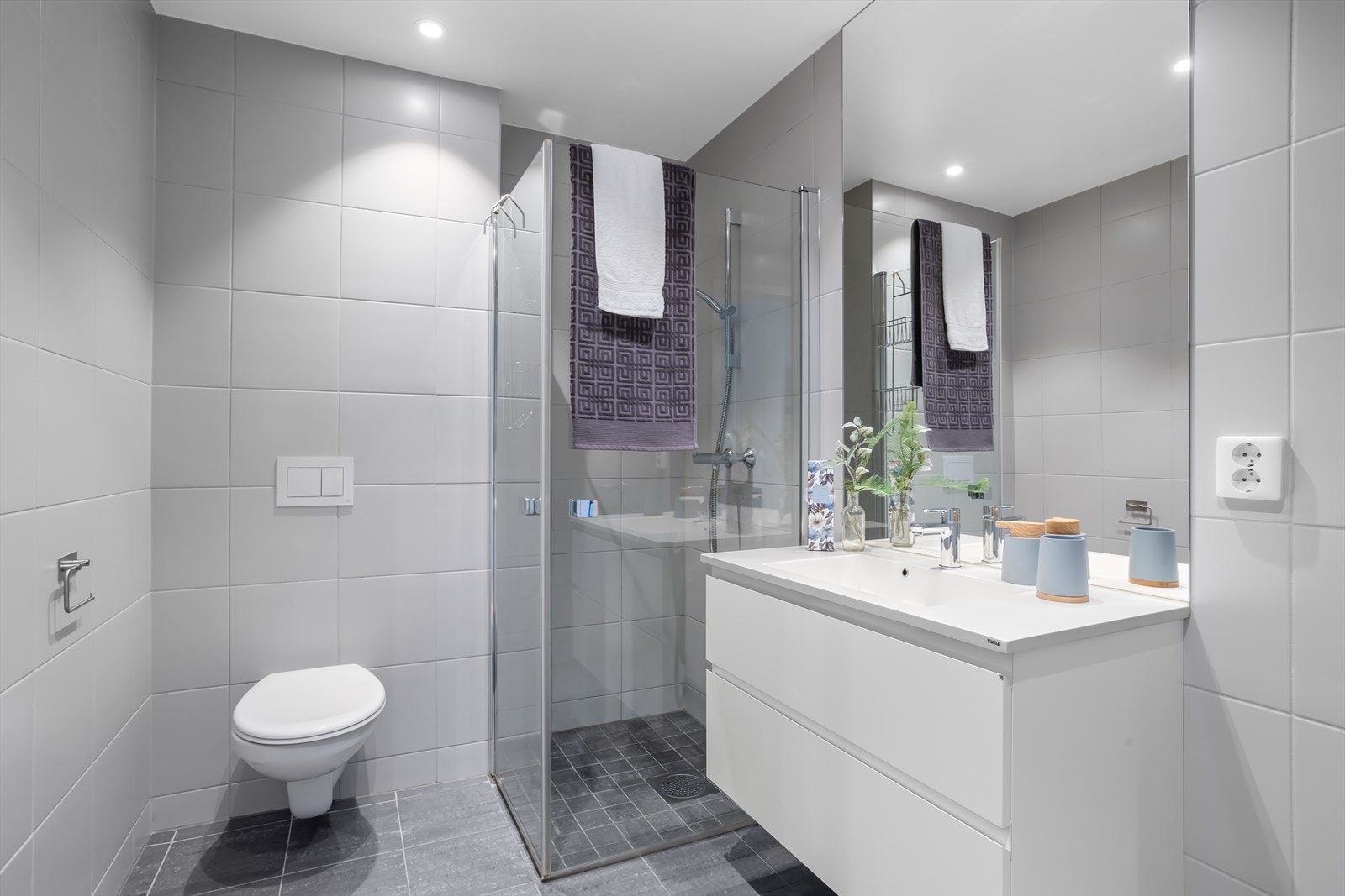 Baderommet har flislagte vegger og flislagte gulv med elektrisk gulvvarme. De matte og lune veggflisene gir badet et varmt og eksklusivt preg. I dusjløsningen er det matchende fliser av mindre dimensjon enn øvrige gulvfliser. Galleribilde