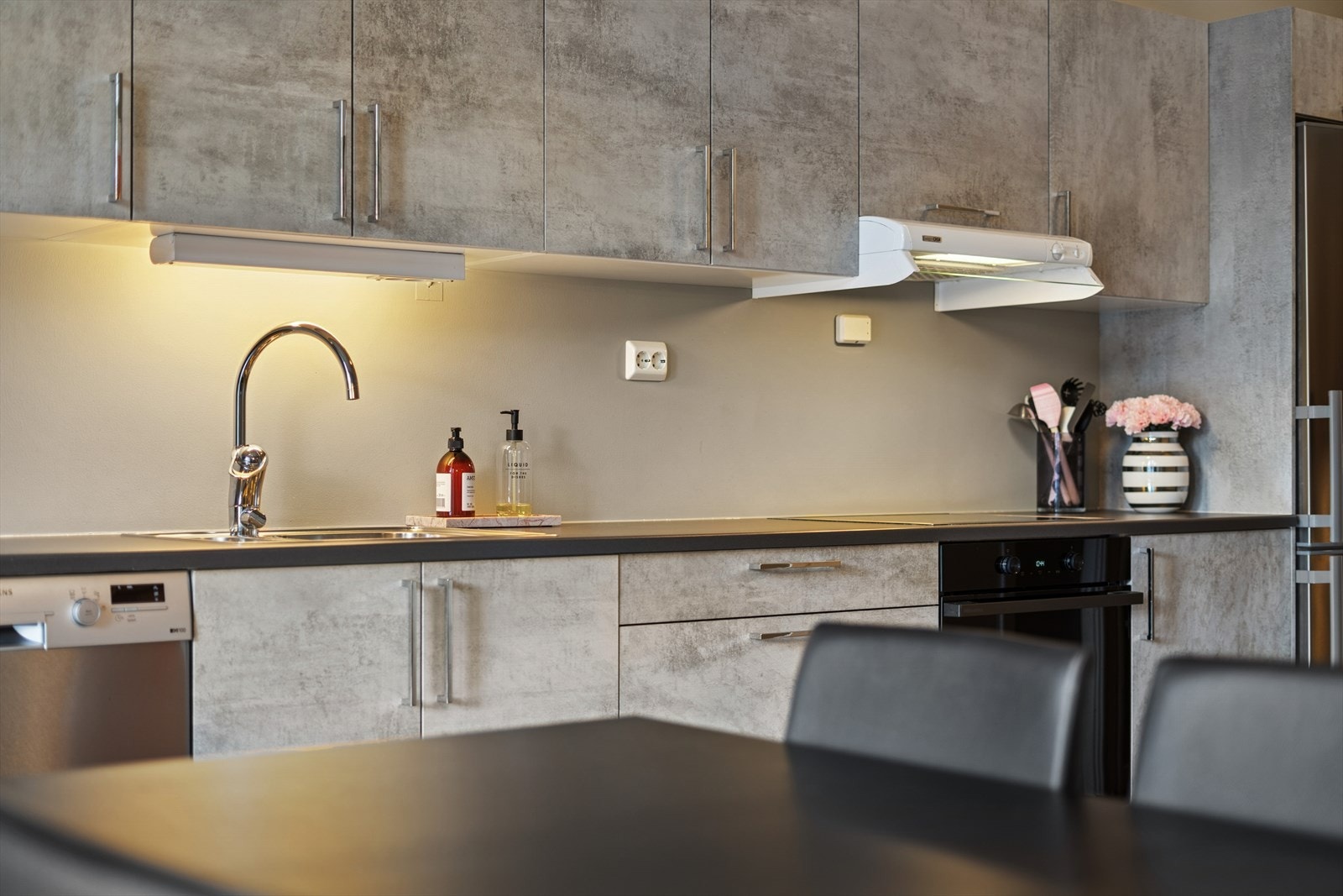 Kjøkkenet er innredet med slette fronter dekorert med grå dekorplast og grå benkeplate i laminat. Et praktisk kjøkken hvor man har godt med skap- og skuffeplass, samt gode arbeidsflater på benk. Galleribilde