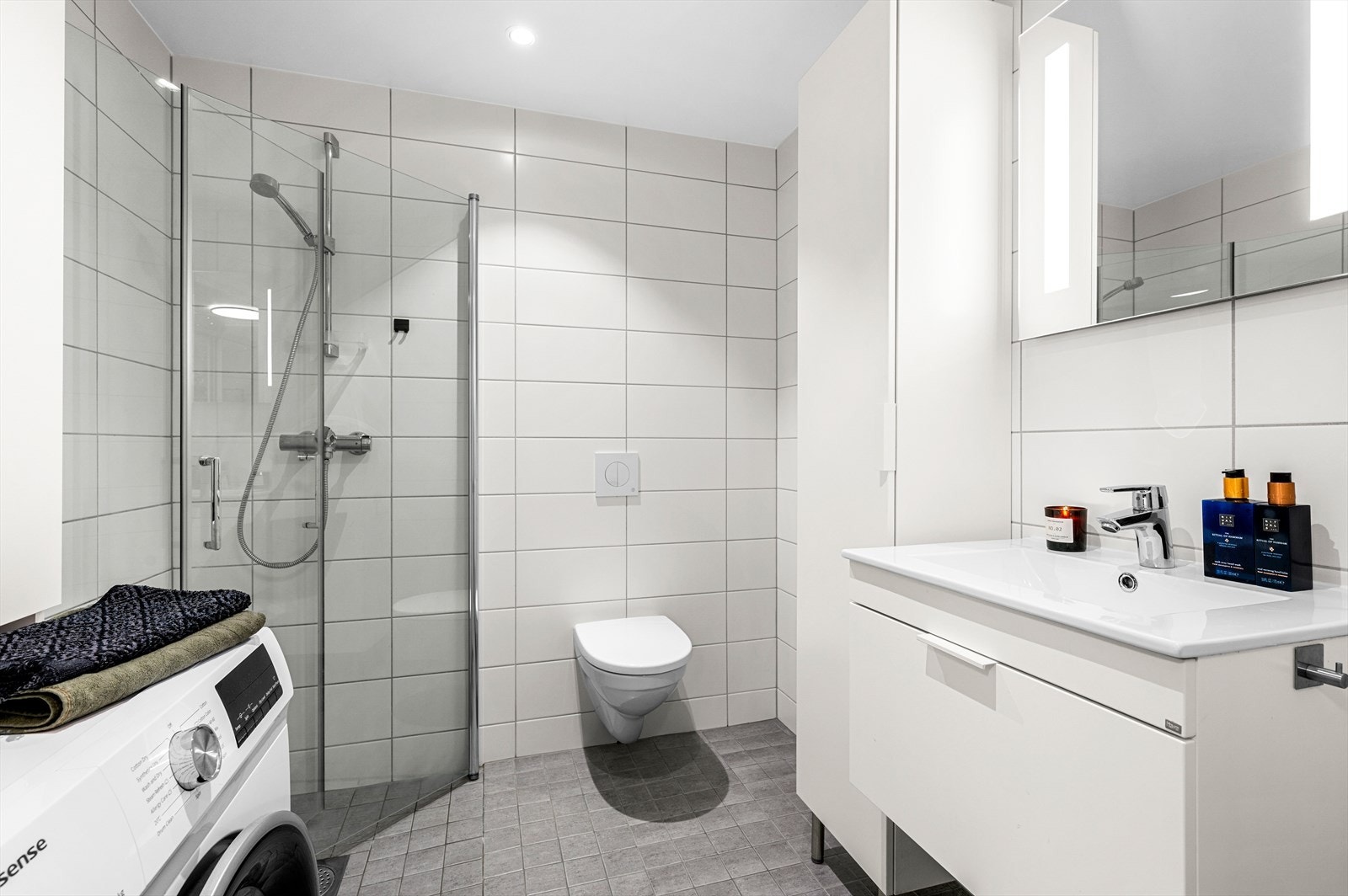 Videre er det et innbydende baderom på 3 m² med dusjhjørne, vegghengt toalett og flott baderomsinnredning. Her er det også opplegg for vaskemaskin. Galleribilde