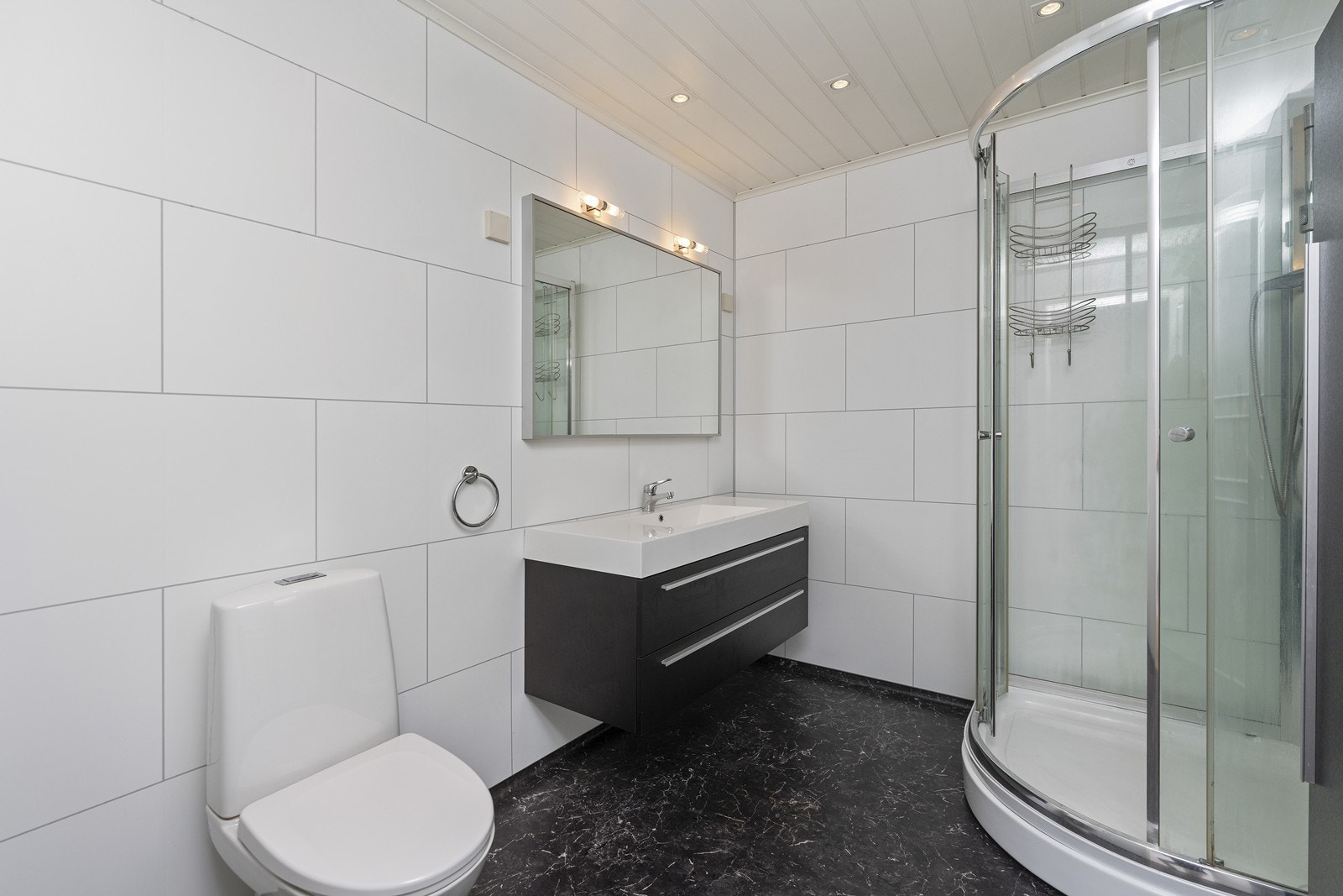 Nyere og tidløst bad med hvite baderomsplater på vegg og mørkt belegg på gulv. Rommet har elektriske varmekabler i gulv, dusjkabinett, innredning med nedfelt servant og toalett. Galleribilde