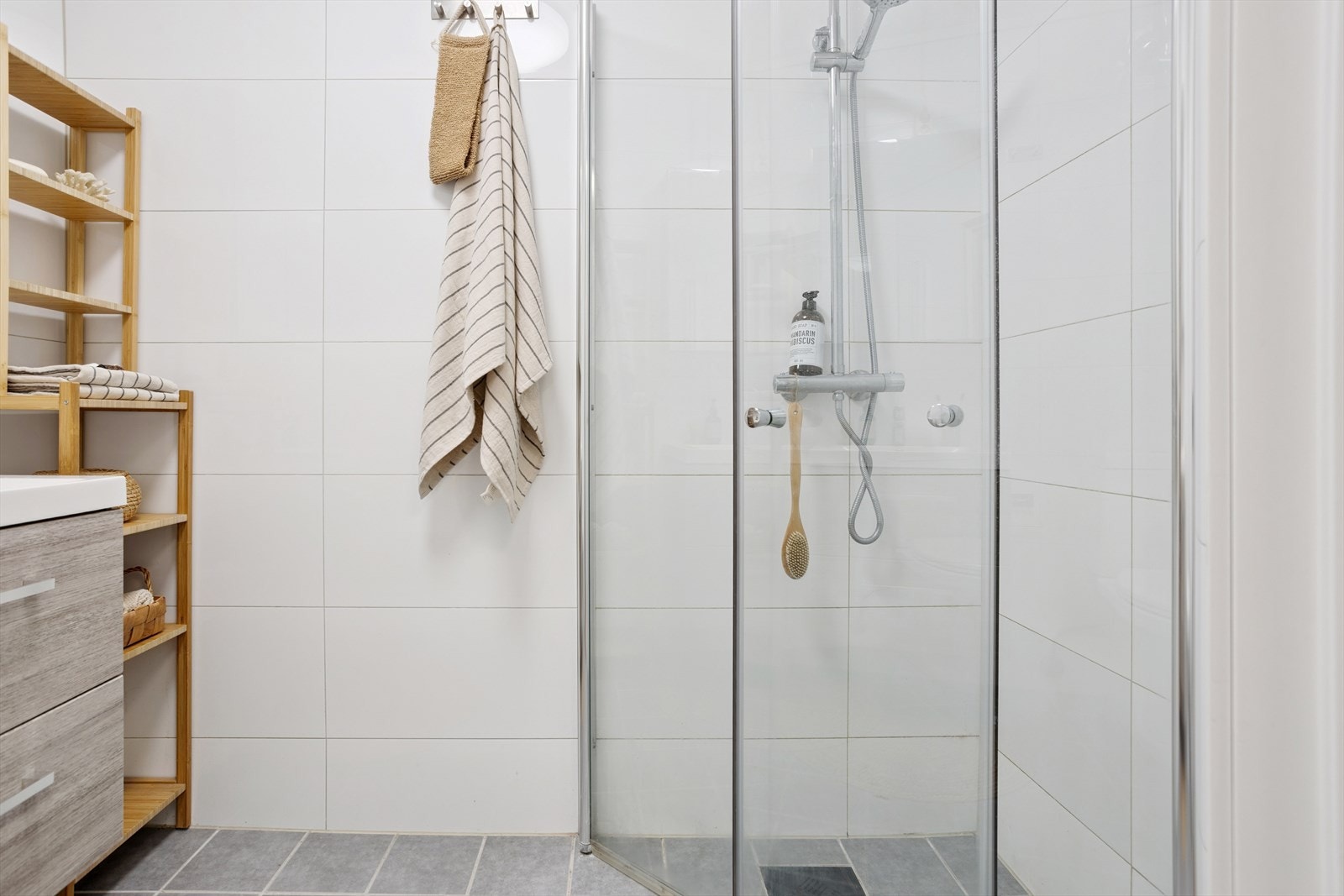 Badet har hvit vask med skapinnredning, overskap med speilfronter, vendbare dusjdører og gulvmontert toalett. Det er i tillegg varme i badegulv. Galleribilde