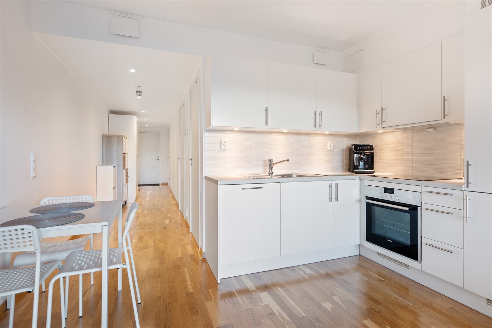 Kjøkkeninnredningen er i praktisk L-form med hvite, slette fronter og laminat benkeplate. Galleribilde