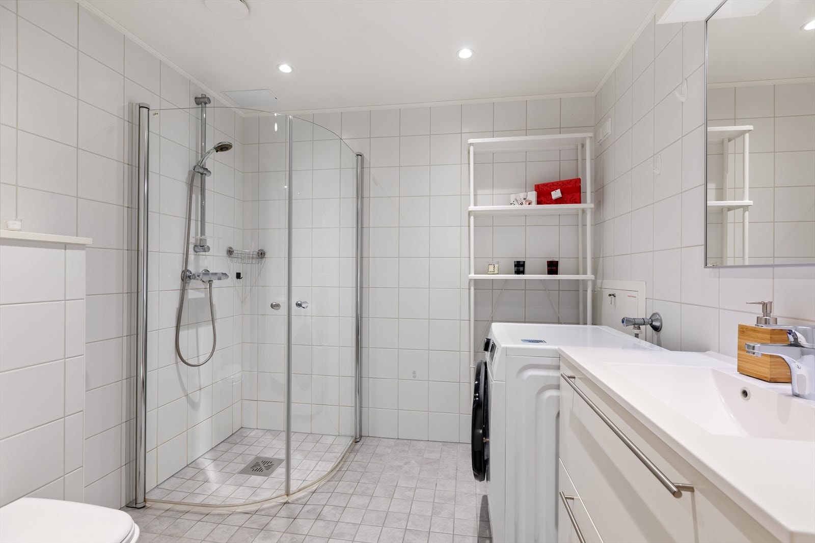 Badet er innredet med vegghengt toalett, dusjhjørne og helservant på skuffeseksjon. Galleribilde