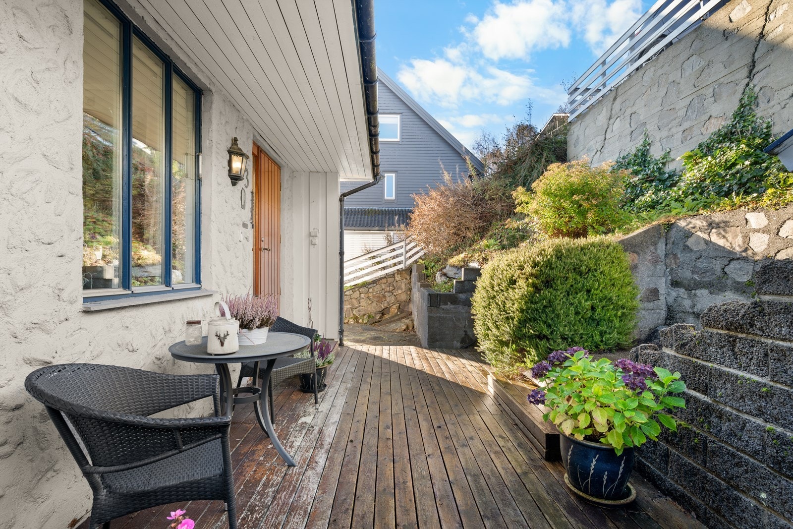 Terrassen danner en lun ramme rundt inngangen, pent omkranset av mur og frodige planter Galleribilde