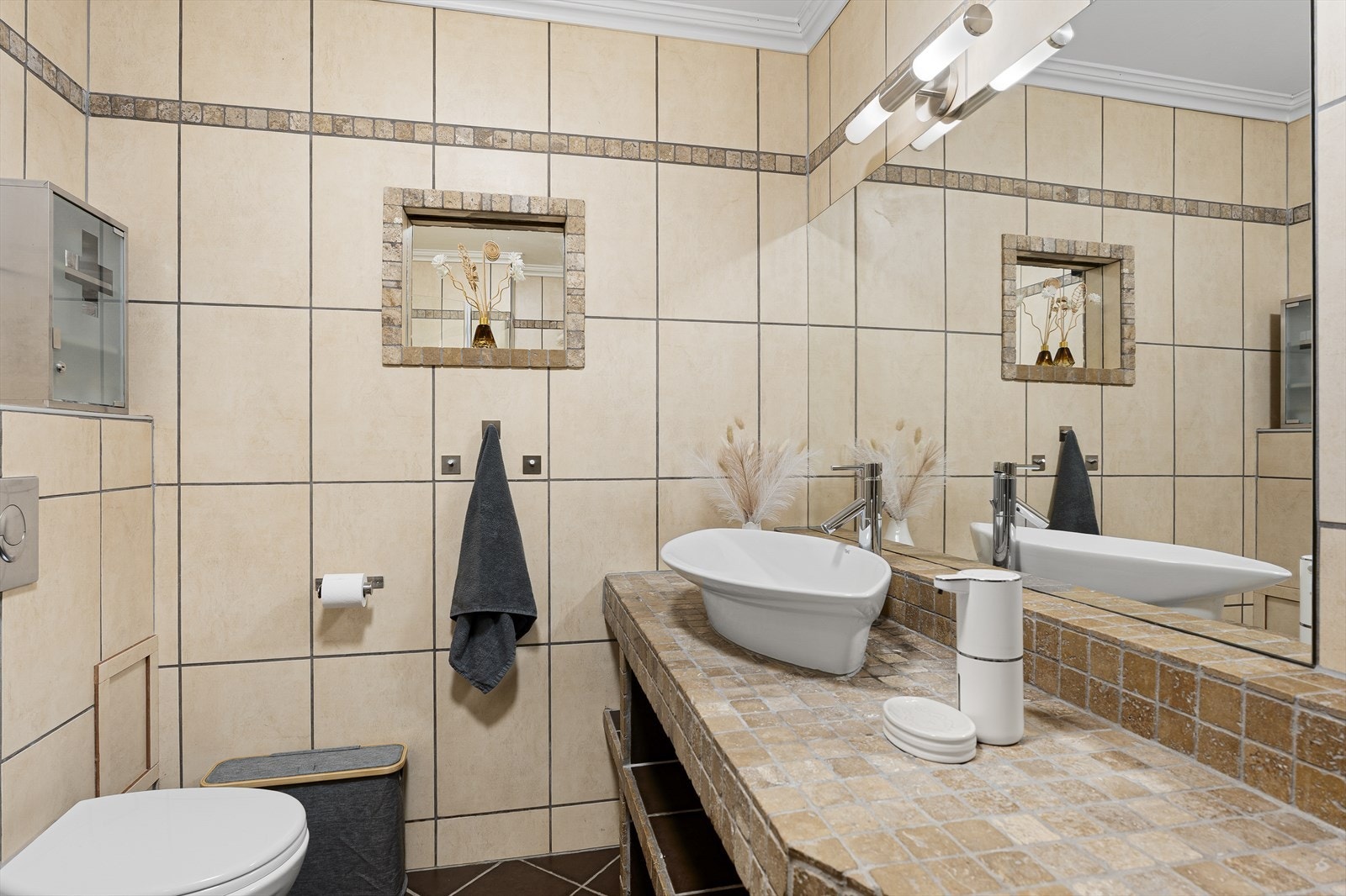 Badet i leiligheten har fliser på gulv og vegger, prefabrikkerte takplater i himling og elektriske varmekabler Galleribilde