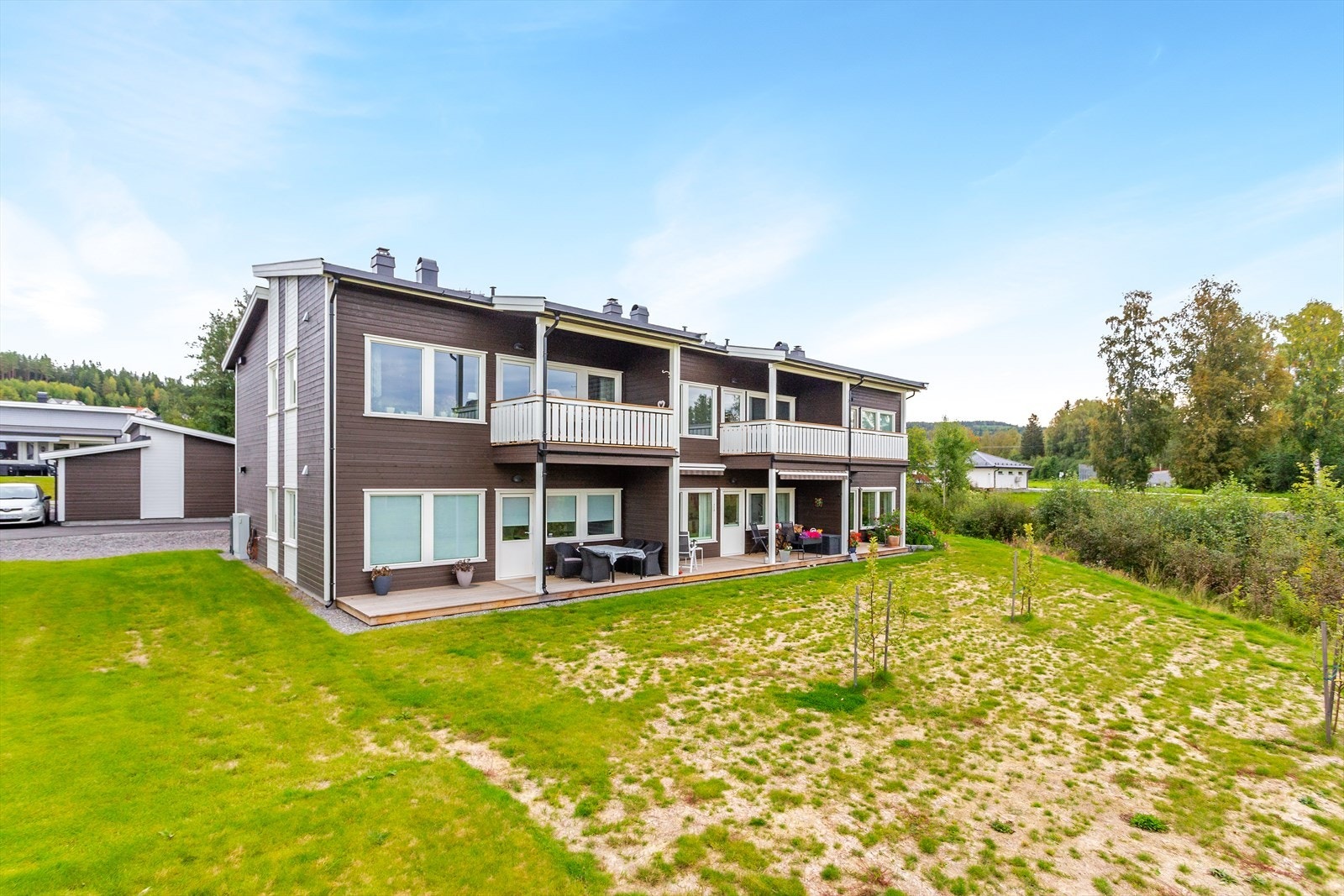 Fasade bakside med balkong. Leiligheten ligger i 2. etasje i en firemannsbolig, og det er adkomst via utvendig trapp. Det følger også carport i front til leiligheten. Galleribilde