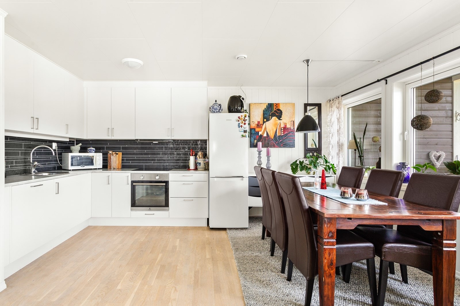 Kjøkkeninnredning med hvite, glatte fronter, laminat benkeplate og plater på vegg mellom overskap og platetopp. Galleribilde