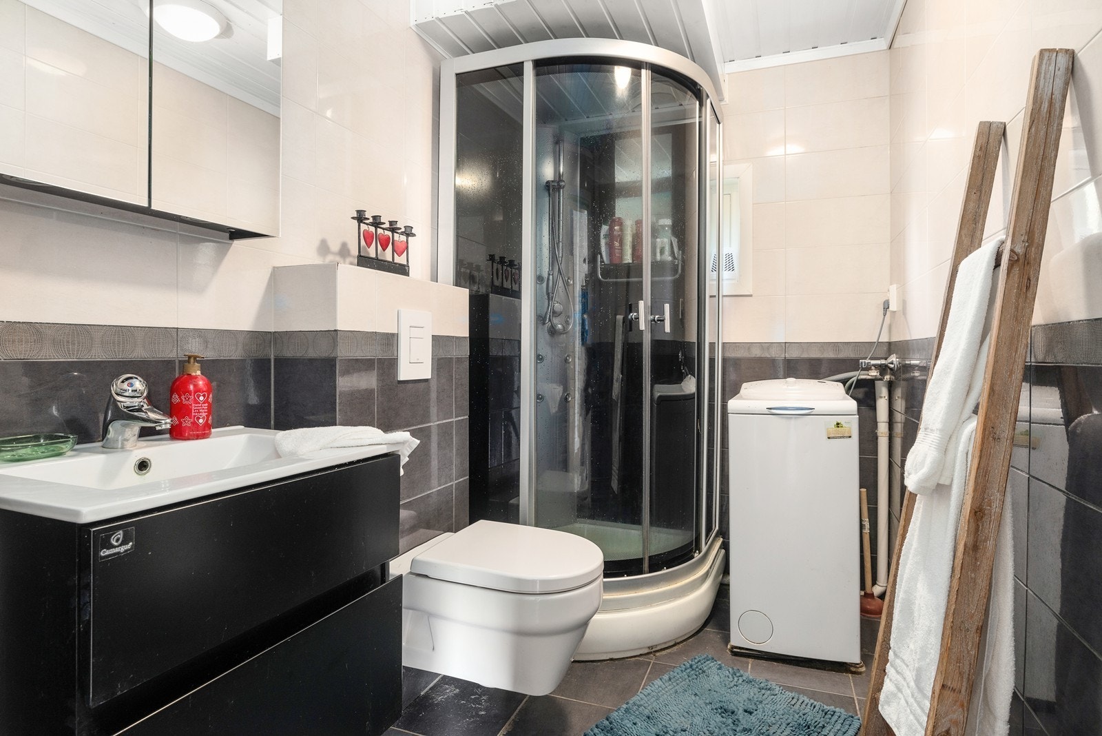 Badet i 1. etasje har flislagt gulv med varmekabler, flislagte vegger og malt panel i himling. Det er opplegg for vaskemaskin og tørketrommel. Badet er fra 2012. Galleribilde