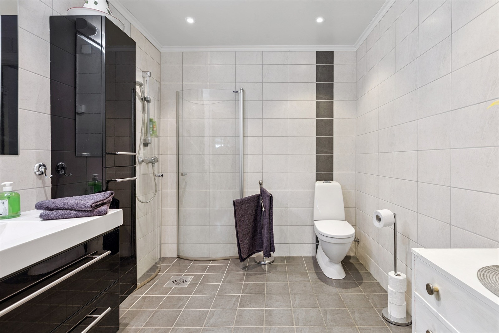 Flislagt bad med vegghengt toalett, dusjhjørne og moderne baderomsinnredning. Galleribilde