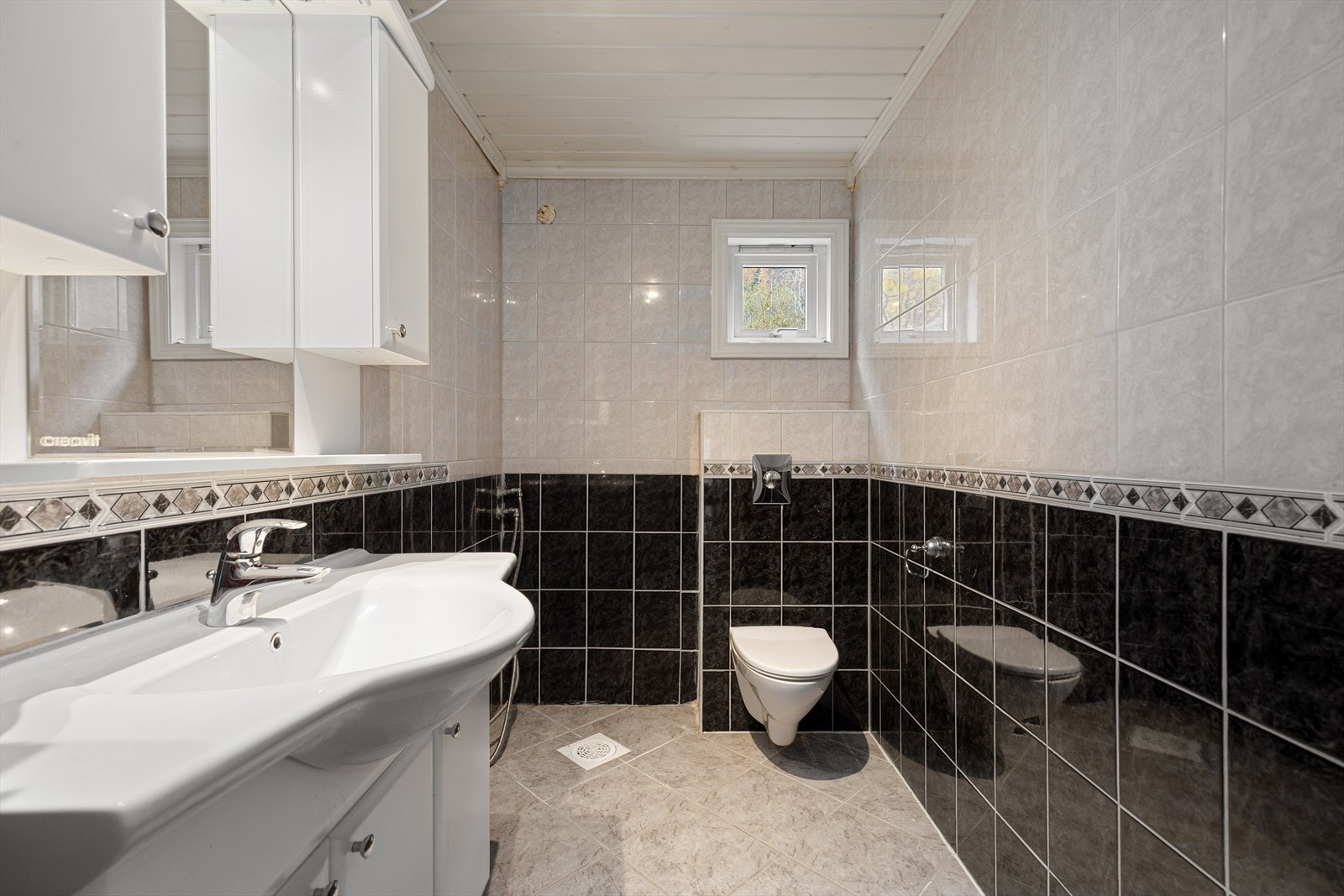 Baderom med fliser på både veggar og golv. badet er utstyrt med dusj, baderomsinnredning med nedfelt servant, og toalett. Galleribilde