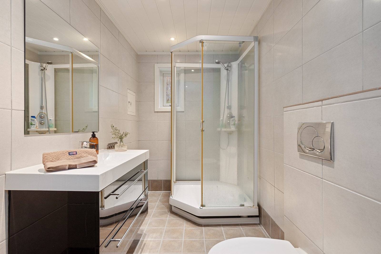 Bad med flislagt golv- og veggar. Badet er innreiia med dusjkabinett, servant og vegghengt toalett. Galleribilde