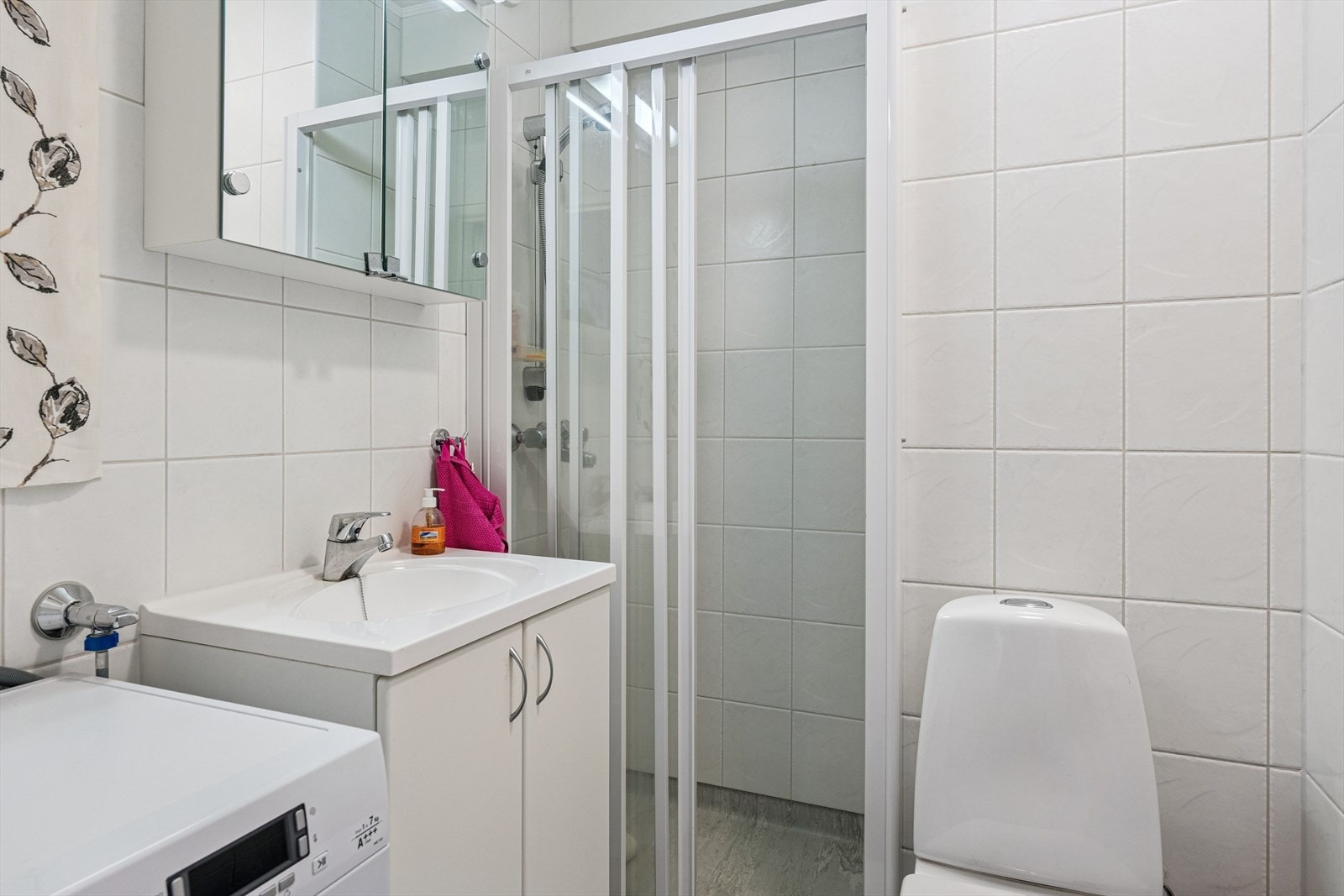 Badet er innredet med klosett, servantinnredning, dusj med glassdør og opplegg til vaskemaskin. Fliser på vegg og belegg på gulv. Galleribilde