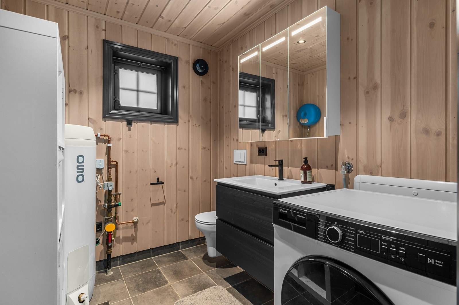 Vaskerom med opplegg for vaskemaskin, toalett og servant på skuffeseksjon. Galleribilde