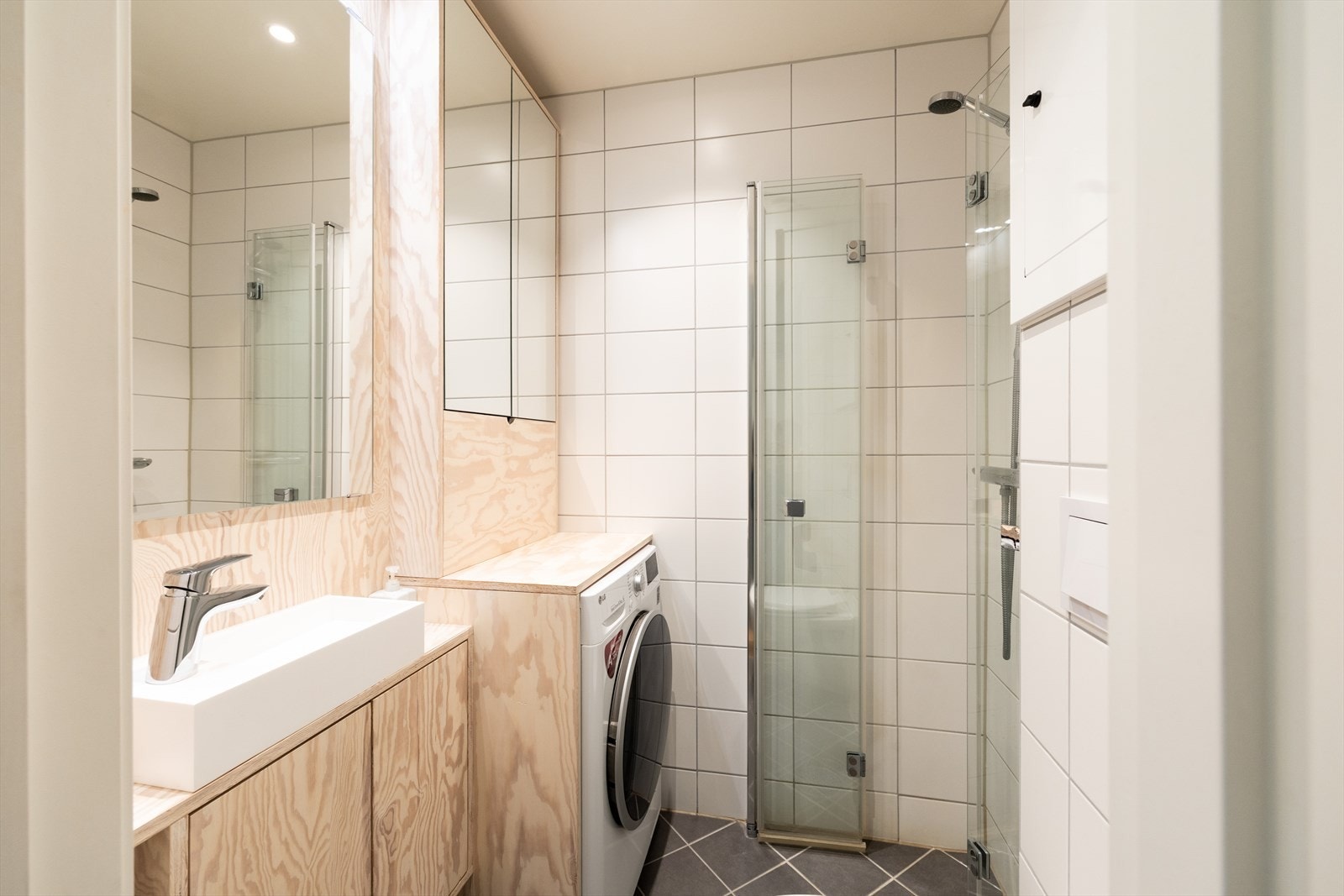 Badet er innredet med vegghengt klosett, servant på innredning og dusjhjørne med innfellbare glassdører. Galleribilde