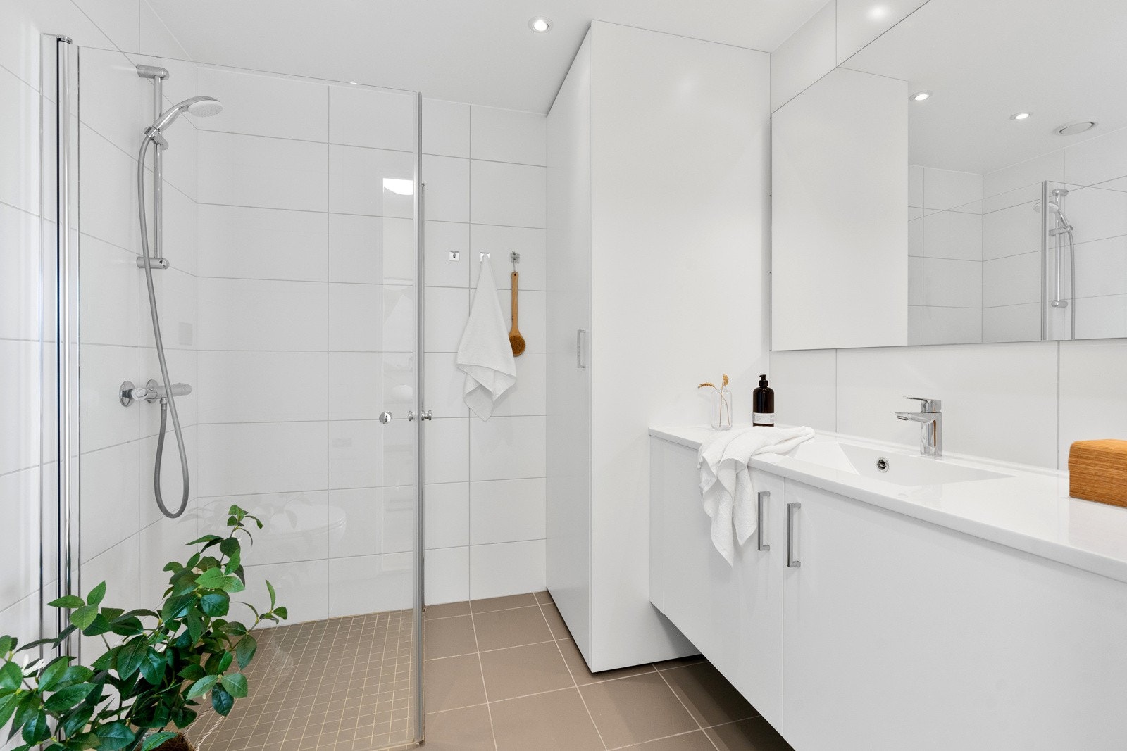 .. et lyst og pent flislagt bad. Badet er utstyt med dusjdører, vegghengt toalett, baderomsinnredning og skap med opplegg til vaskemaskin. Galleribilde