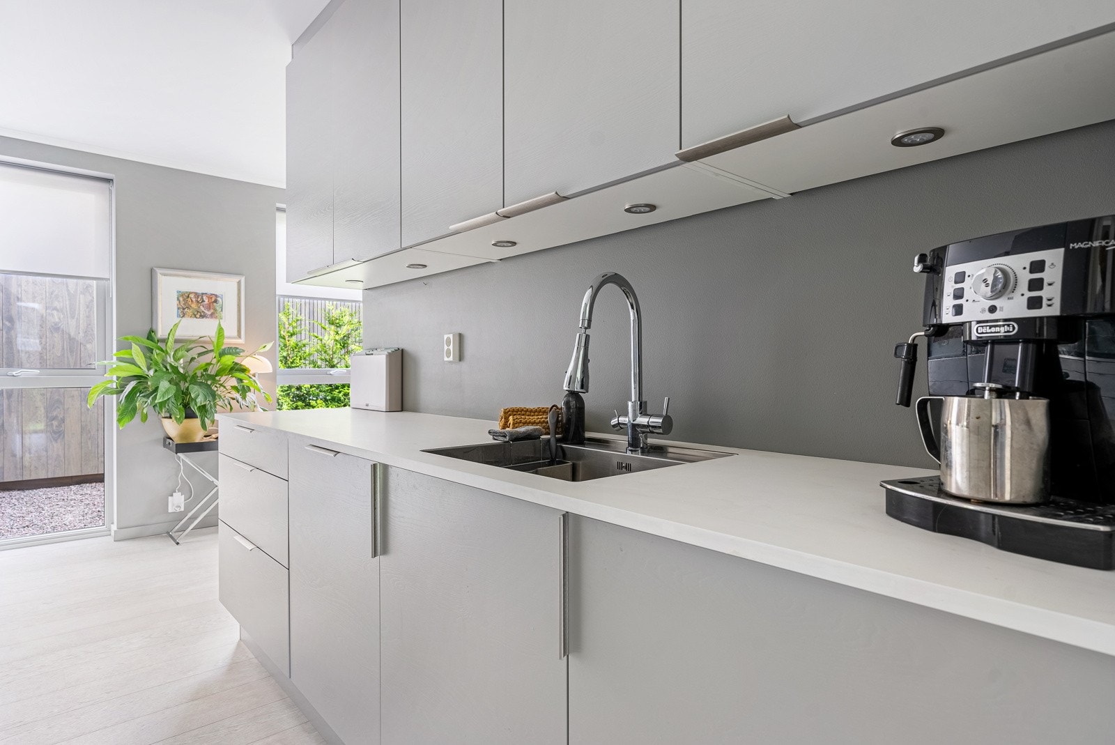 Innredningen er oppført langs to vegger, med grå, glatte fronter, hvit benkeplate av laminat og nedfelt oppvaskkum med pent armatur. Galleribilde