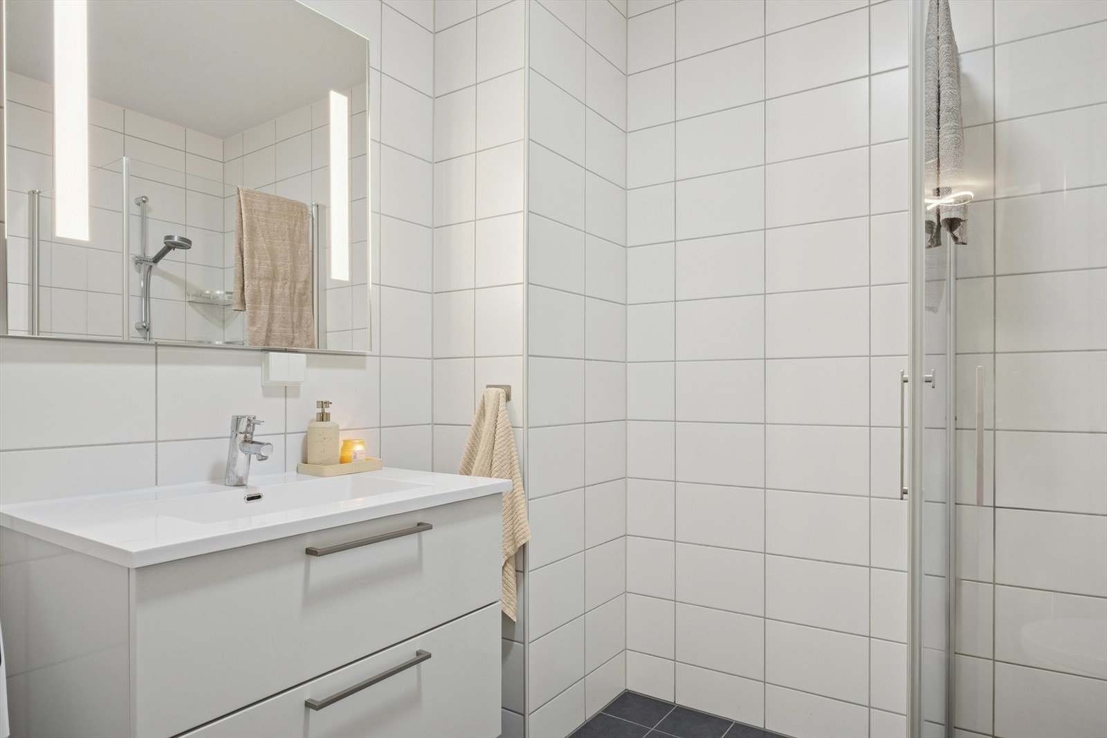 Badet er innredet med baderomsinnredning, speil med overbelysning, dusjgjørne, vegghengt toalett og opplegg for vaskemaskin. Galleribilde