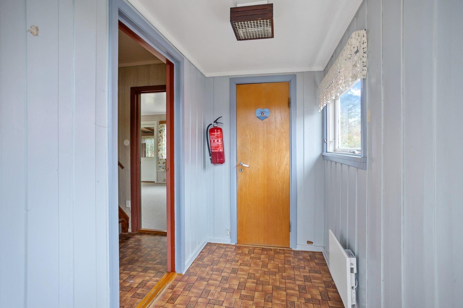 Hjemmets inngangsparti har adkomst trapp fra gårdsplassen på eiendommen. Vel innenfor boligens nye hovedinngangsdør (2024), møter man husets entre med tilknyttet toalettrom. Galleribilde