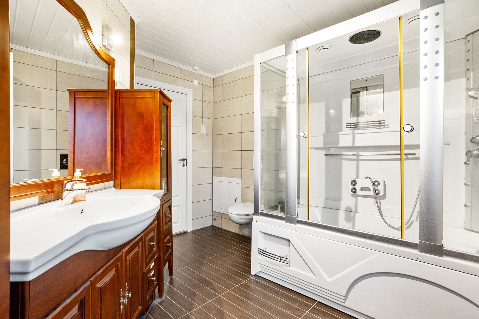 Badet er innredet med servant i baderomsinnredning med speil, stort dusjkabinettbadekar, vegghengt toalett og opplegg for vaskemaskin. Galleribilde