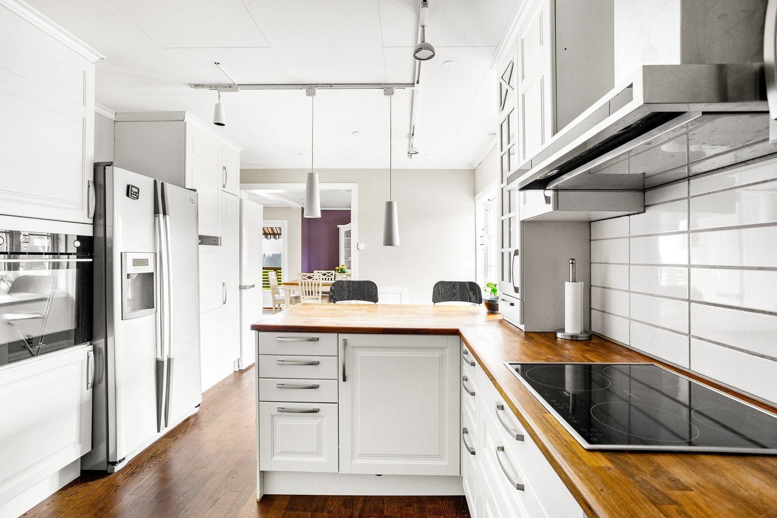 Flott kjøkken med integrerte hvitevarer, herunder stekeovn, induksjonsplatetopp, oppvaskmaskin og frittstående kombiskap. Galleribilde