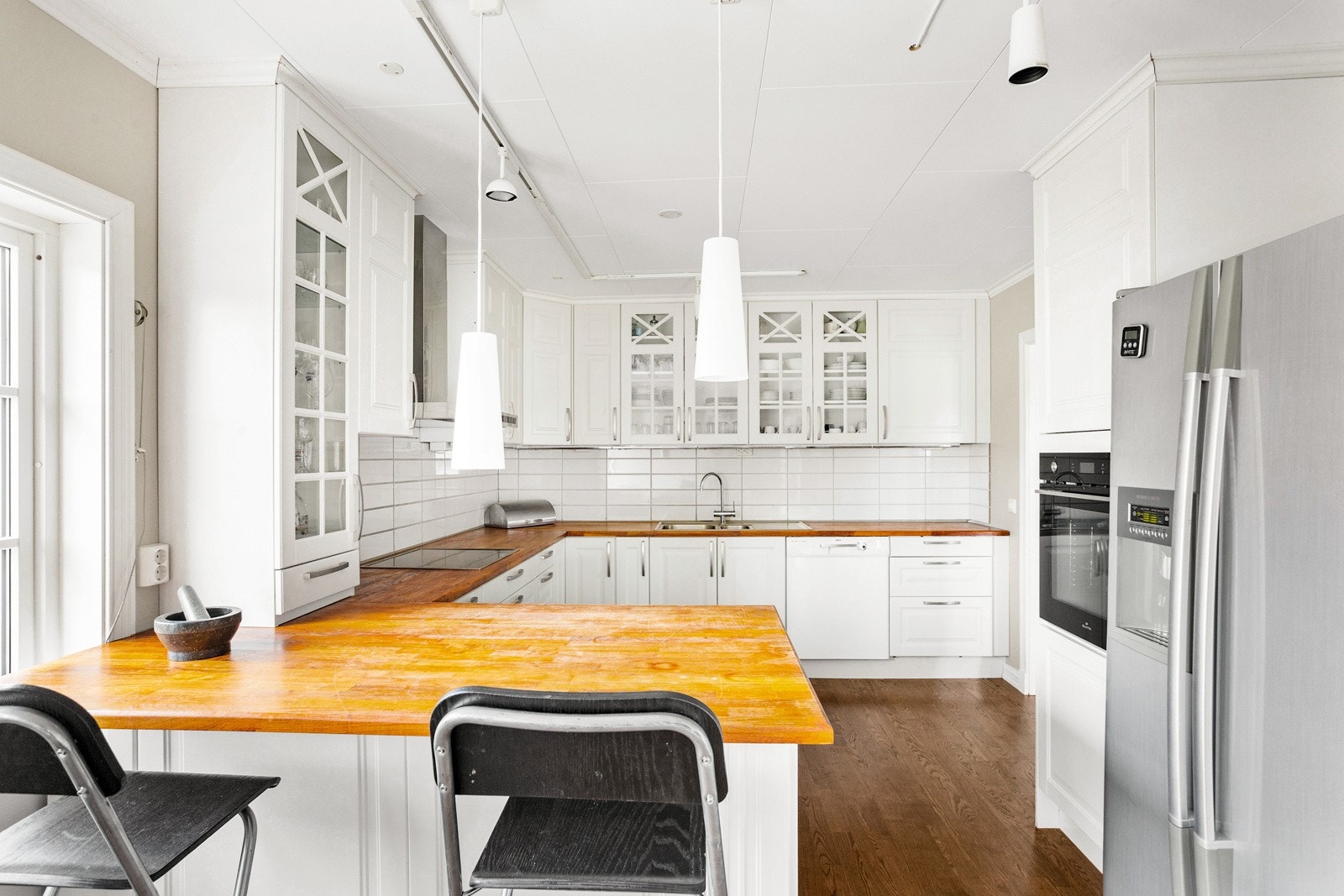 Kjøkkeninnredning med hvite, profilerte fronter, heltre benkeplate og praktisk bar-løsning. Galleribilde