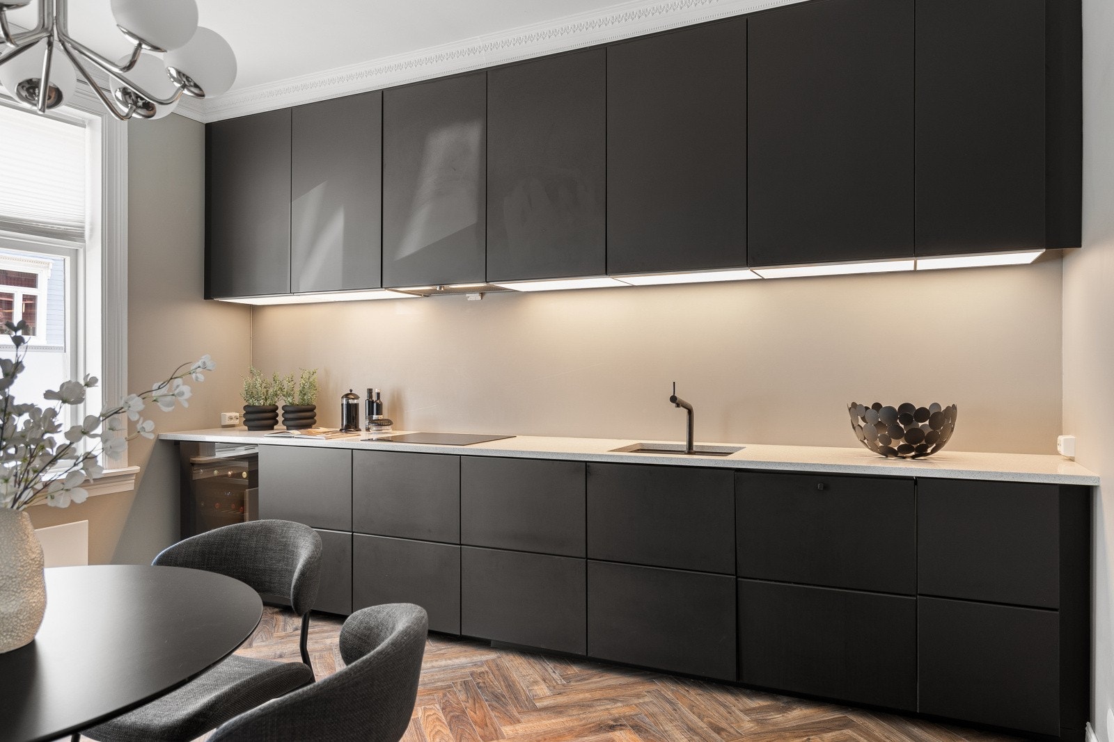 Her får du gode oppbevaringsmuligheter på begge sider av kjøkkenet. På denne siden er det integrert platetopp, oppvaskmaskin og et lekkert vinskap som fullfører det stilsikre uttrykket. Galleribilde