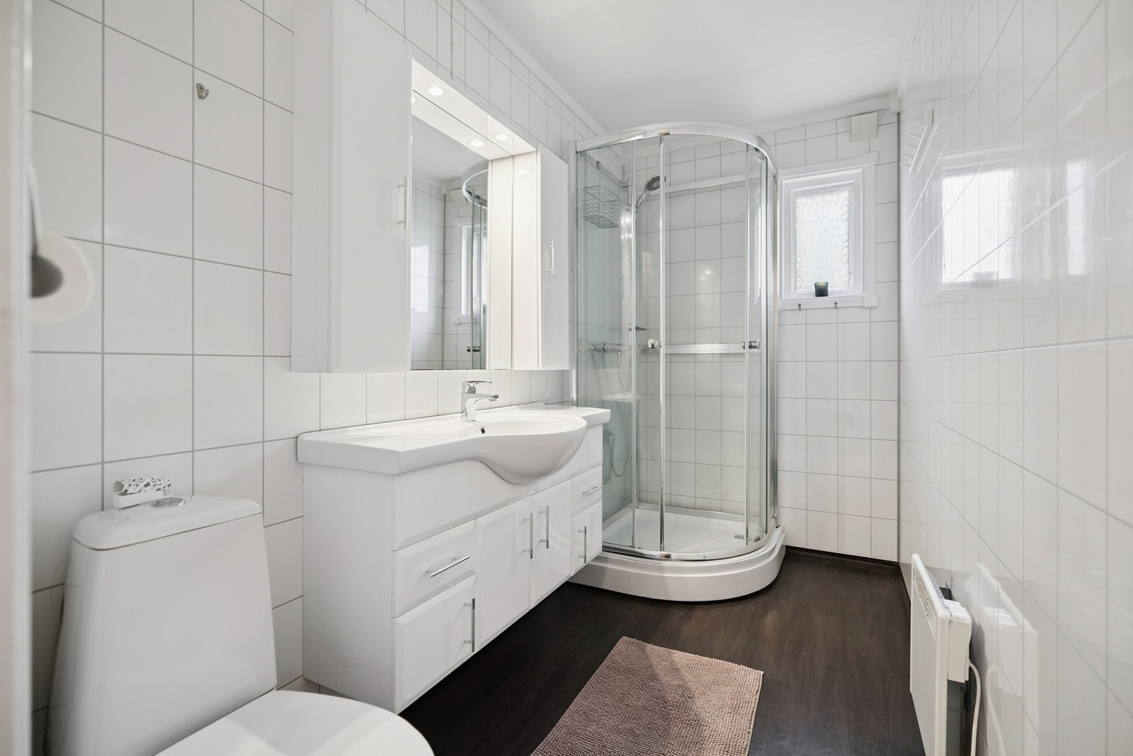 Stilren baderomsinnredning med heldekkende servant og overskap med speil og integrert belysning. Galleribilde