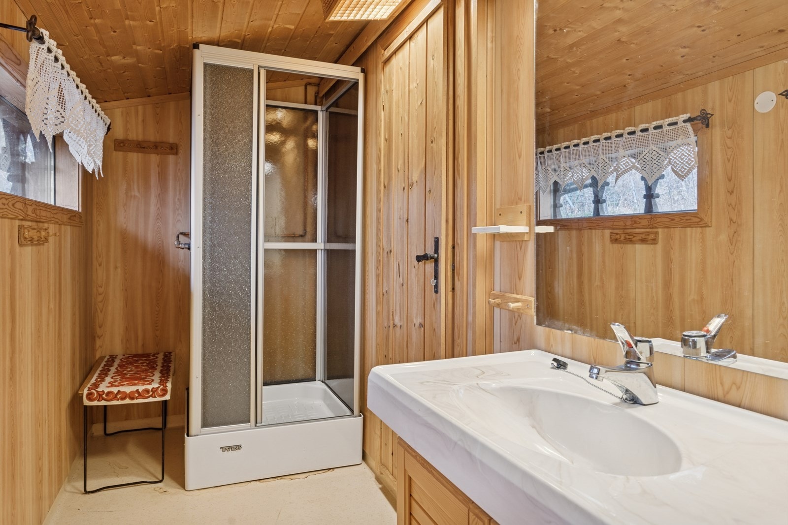 Badet har panel på vegger og flislagt gulv med dusjkabinett og mekanisk avtrekk. Galleribilde