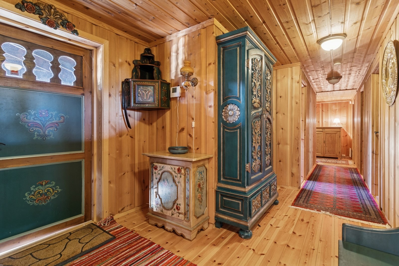 Panelte vegger og gulv i tre skaper en varm atmosfære i gangen, med dekorative detaljer på møbler og dører. Galleribilde