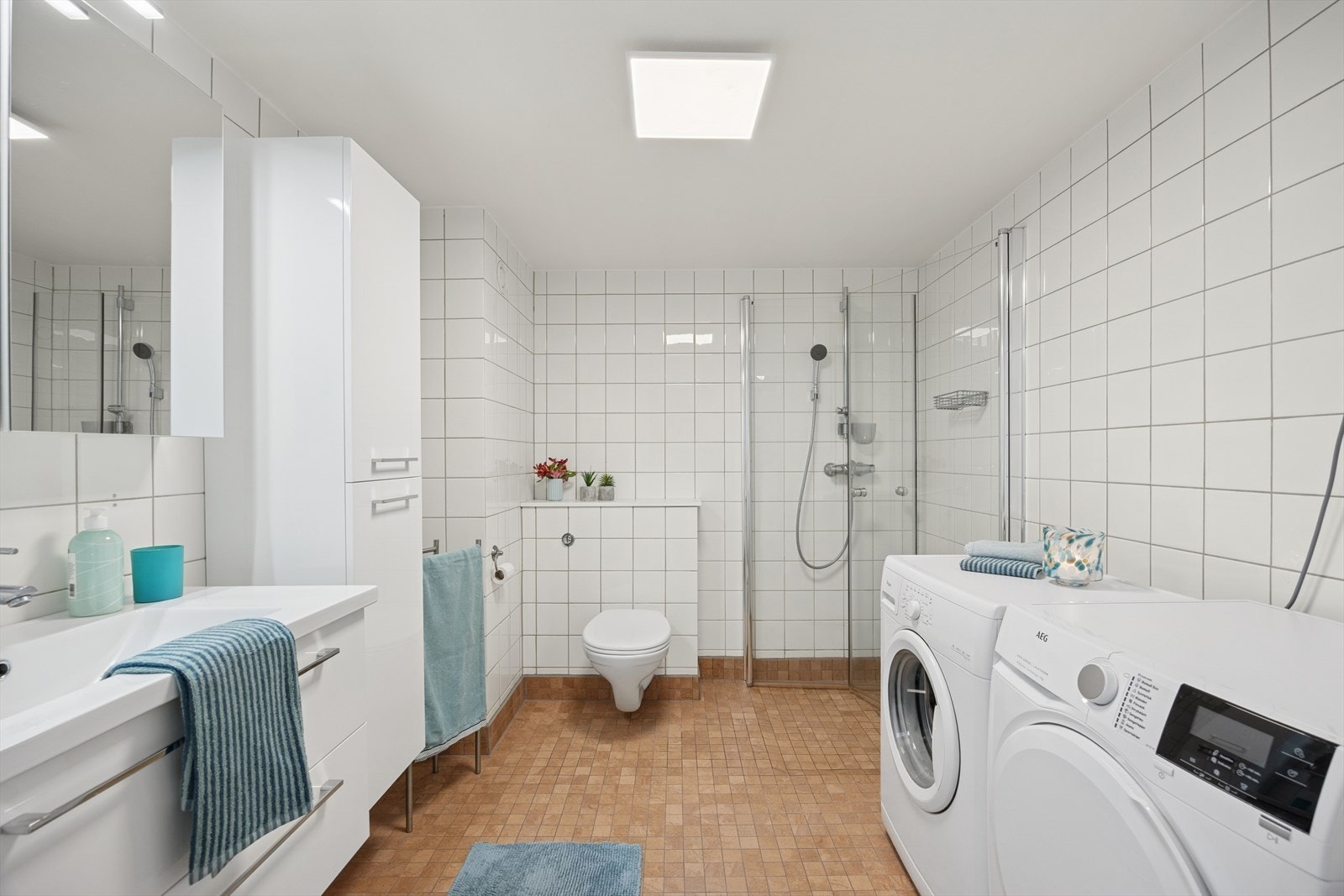 Baderommet er innredet med dusjhjørne, servantløsning m/ under- og overskap, høyskap, vegghengt toalett, samt opplegg for vaskemaskin og tørketrommel Galleribilde