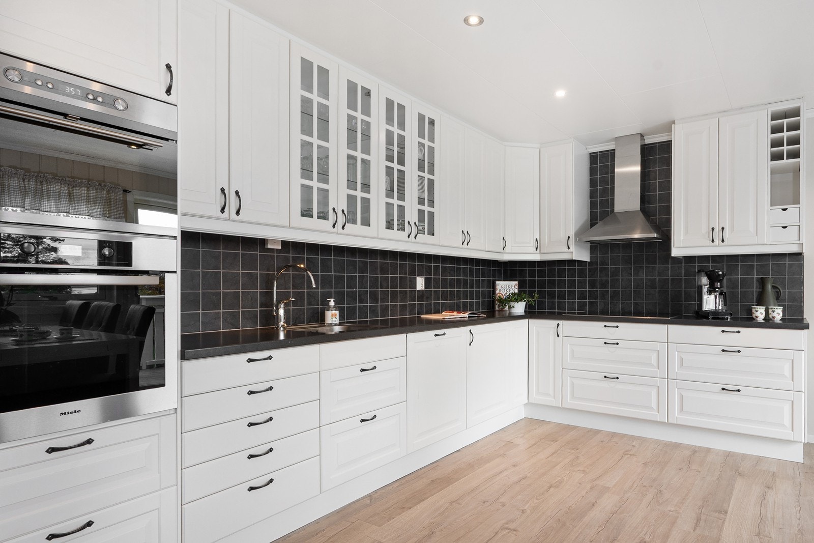 Kjøkkenet har en gjennomtenkt og funksjonell utforming med hvite, profilerte fronter og mørk laminat benkeplate. Galleribilde