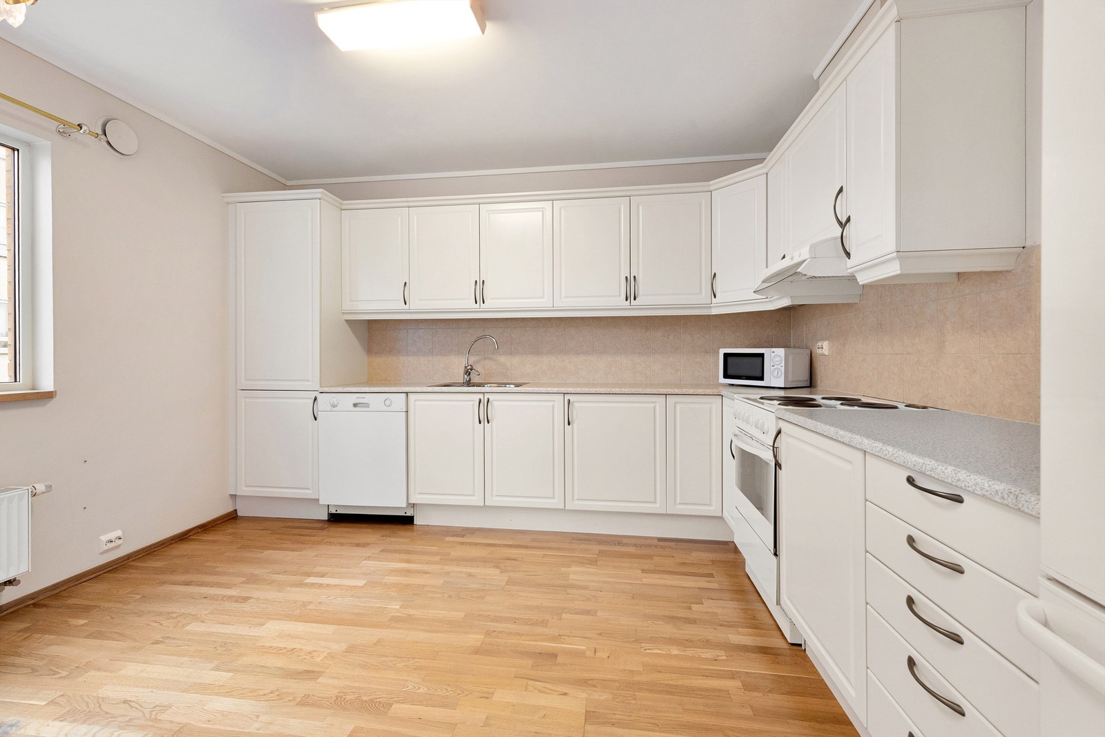 Romslig kjøkkeninnredning fra byggeår med frittstående hvitevarer Galleribilde