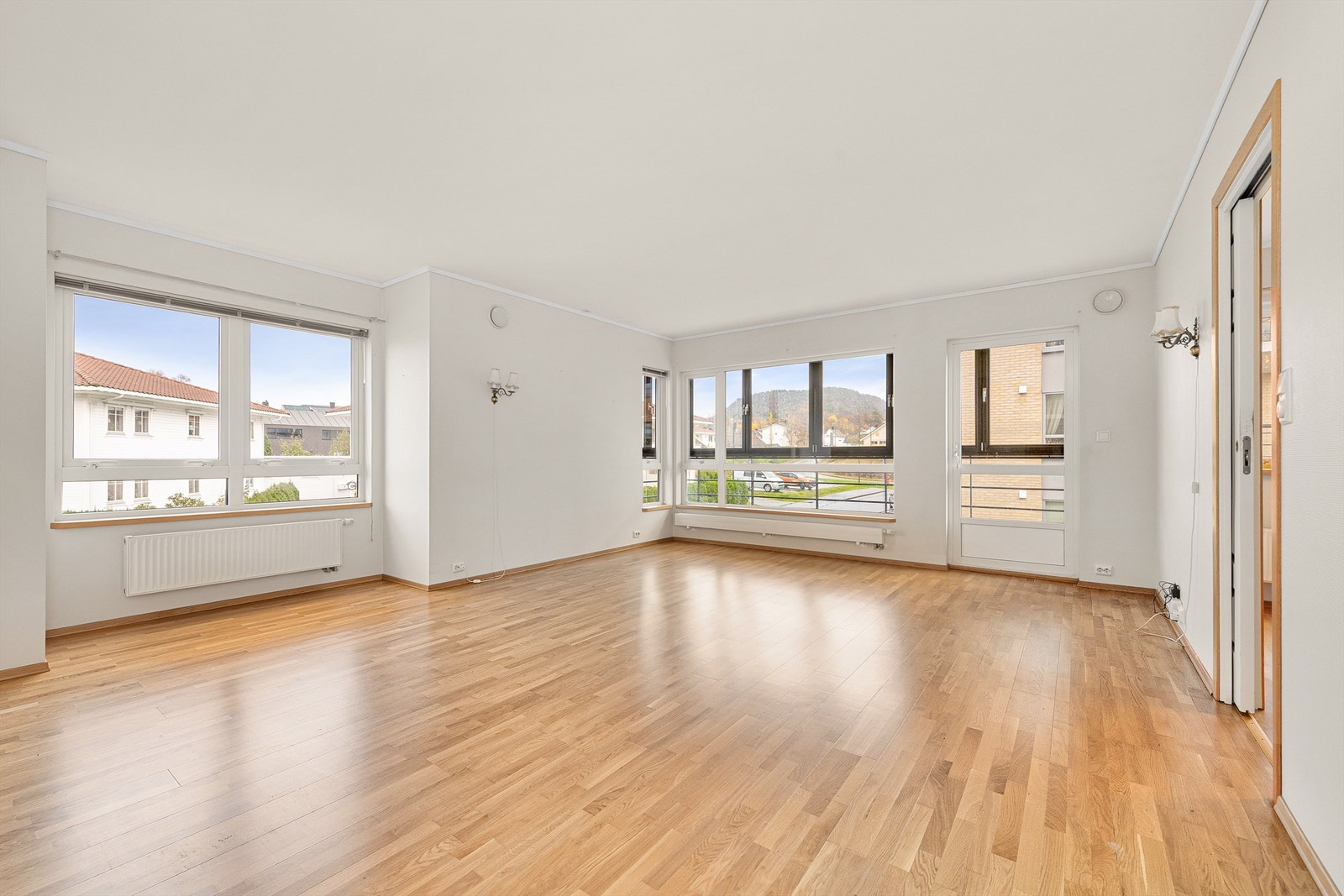 Romslig stue med lyse overflater og utgang til innglasset balkong. Godt med naturlig lysinnslipp fra vinduer Galleribilde