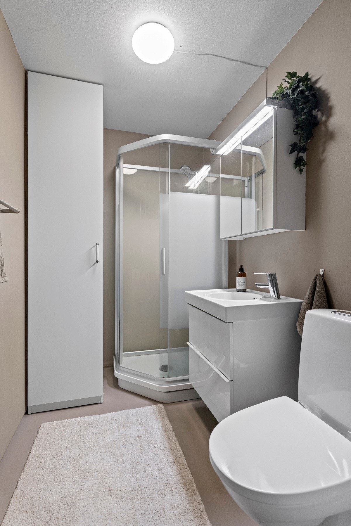 Baderomsinnredningen består av nedsenket porselenvask med ettgreps blandebatteri, speilskap, dusjkabinett og gulvstående toalett Galleribilde