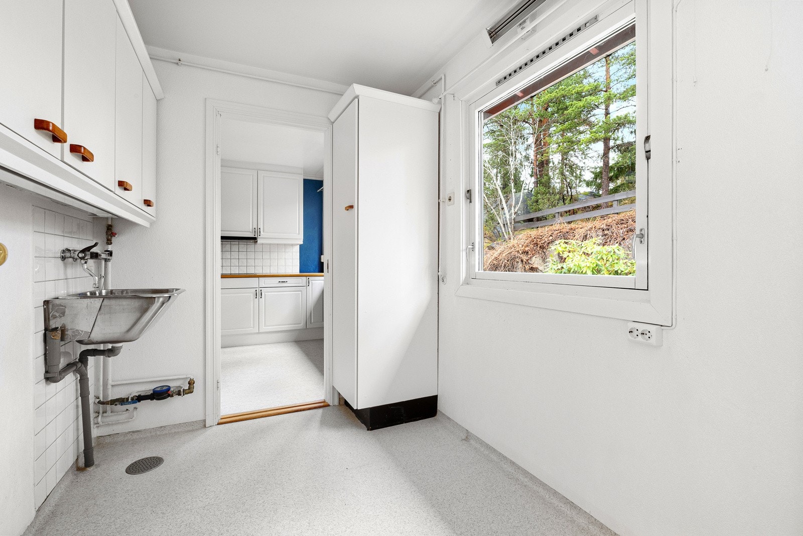 Vaskerom med utslagsvask, opplegg for vaskemaskin og skap til oppbevaring. Synlige vann- og avløpsrør, hovedstoppekran og varmtvannsbereder er plassert her. Galleribilde