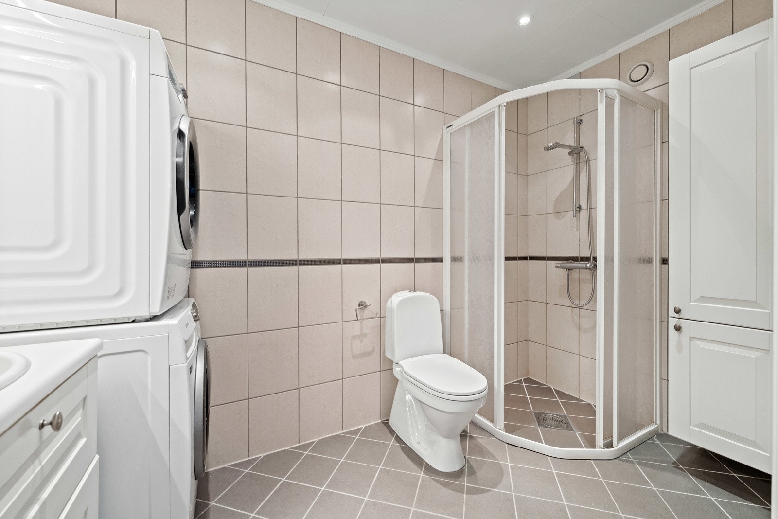 Rommet har gulv- og veggfliser i harmonerende gråtoner og grå flisbord langs brystning Galleribilde