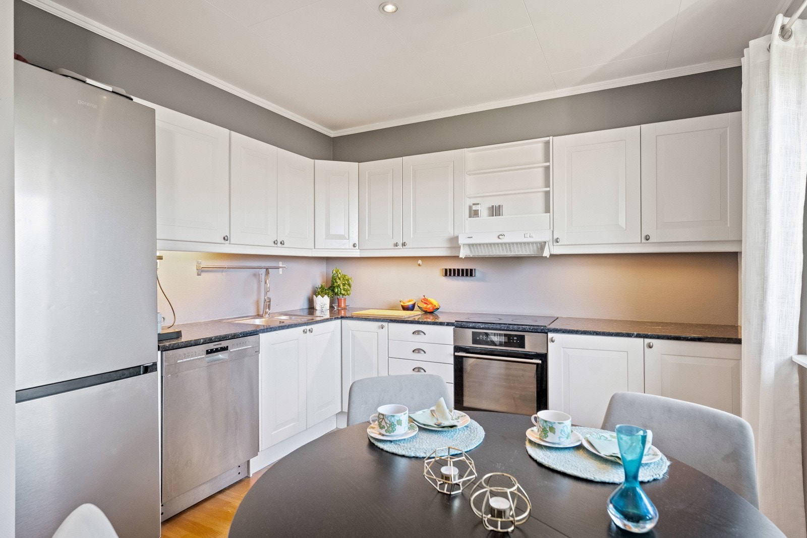 Innredningen har hvite profilfronter, sorte laminatbenkeplater og nedfelt vaske- og skyllekum i rustfritt stål. Det pene Sigdal-kjøkkenet er designet i en hendig L-form og har god skap- og benkeplass Galleribilde