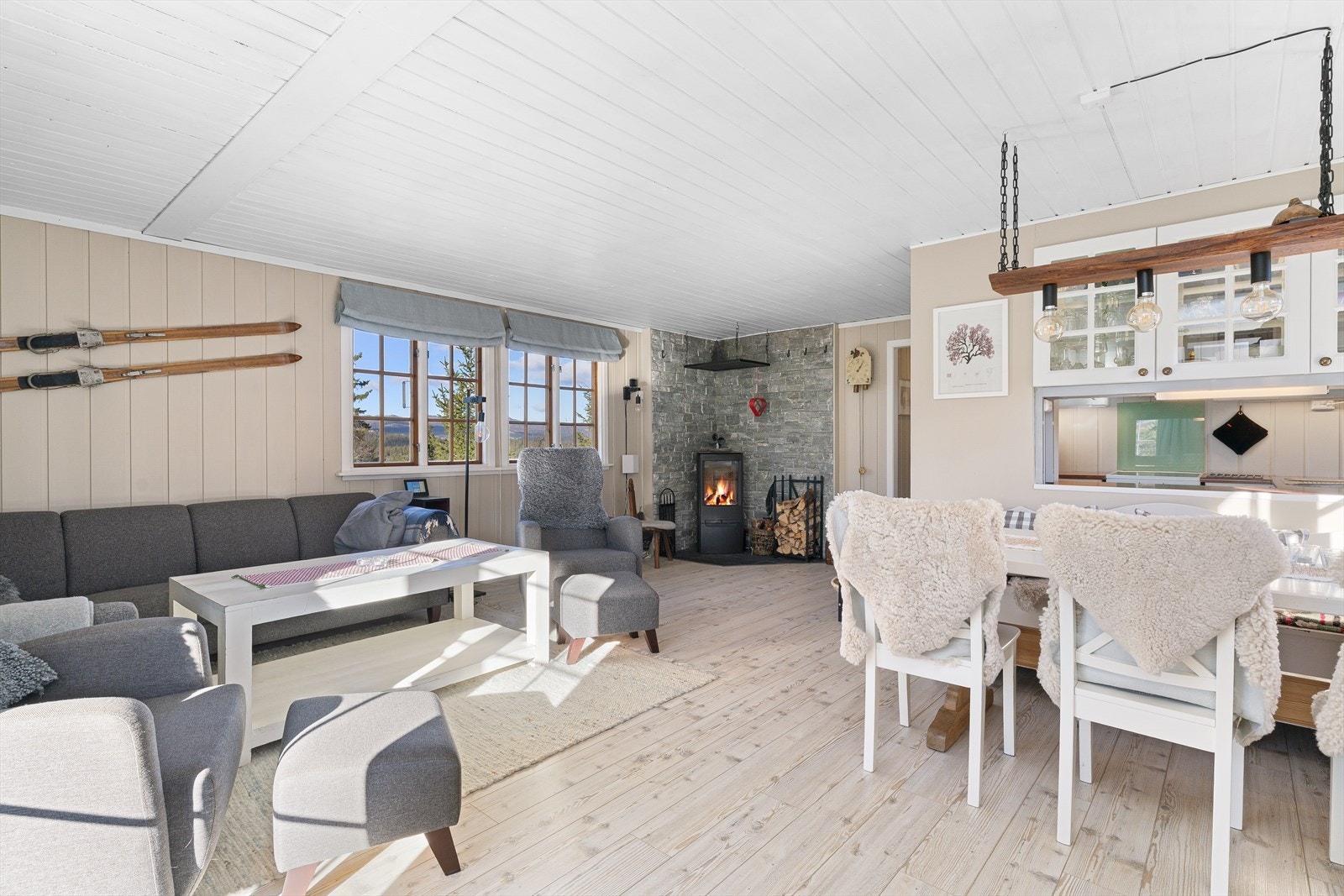 Lys og innbydende stue med gulv av 1-stavs laminat og lysmalt panel på vegg. Galleribilde