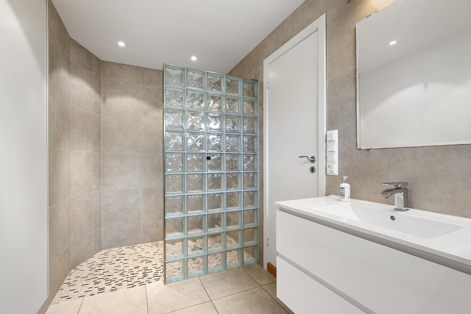 Bad/wc fra 2010 med fliser på gulv og gulvvarme. Våtrommet er utstyrt med baderomsinnredning med servant, speil, lys, dusjhjørne med glassbyggerstein og vegghengt toalett Galleribilde