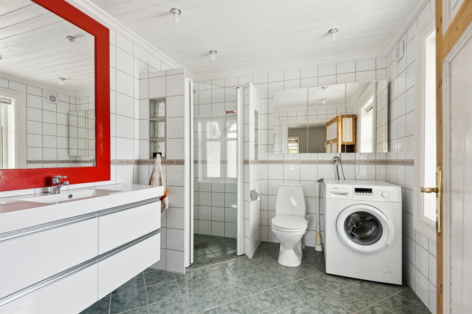 Flislagt bad med plass til vaskemaskin. Heldekkende servant og praktiske løsninger. Galleribilde