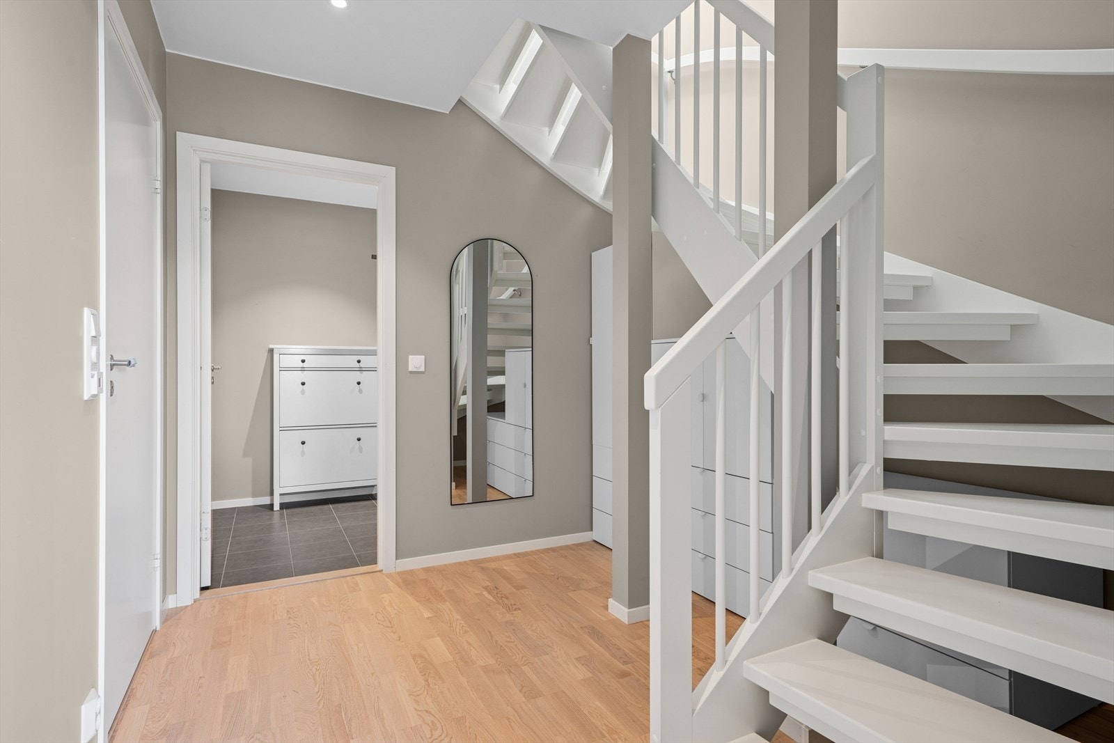 Romslig trappegang som binder etasjens rom sammen og som tilbyr ytterlig oppbevaringsplass under en lys, pen trapp. Galleribilde