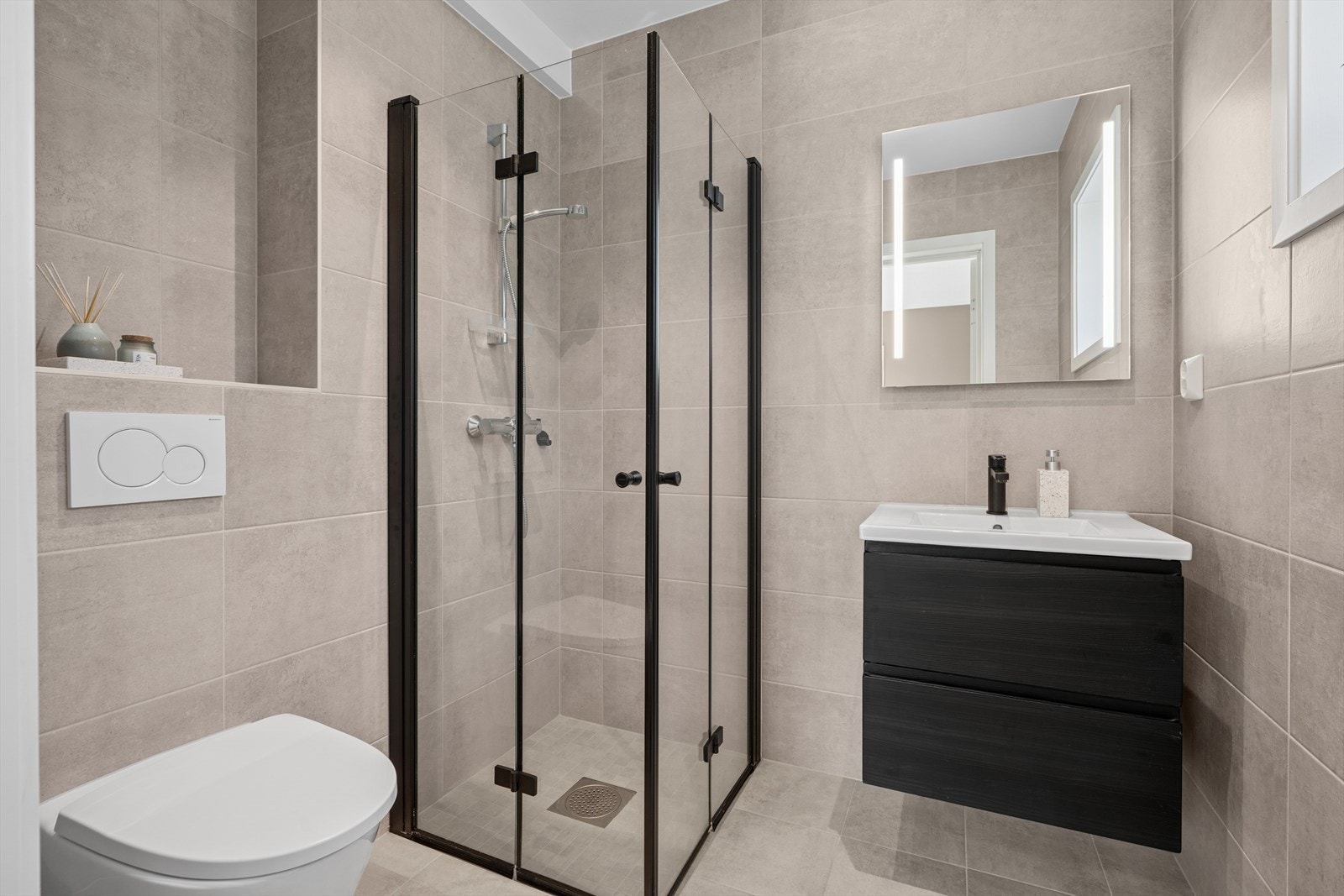 Eget delikat baderom med delikat flisvalg og varmekabler i gulv. Nedfelt servant, veggmontert toalett og nedsenket dusjhjørne med dører i herdet glass. Galleribilde